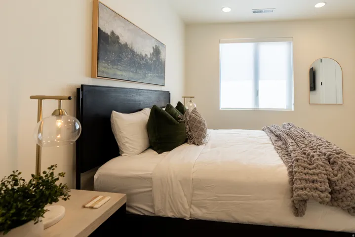 Recessed lighting, window with roller shade, arched wall mirror, dark wood-finish headboard, and light-toned walls