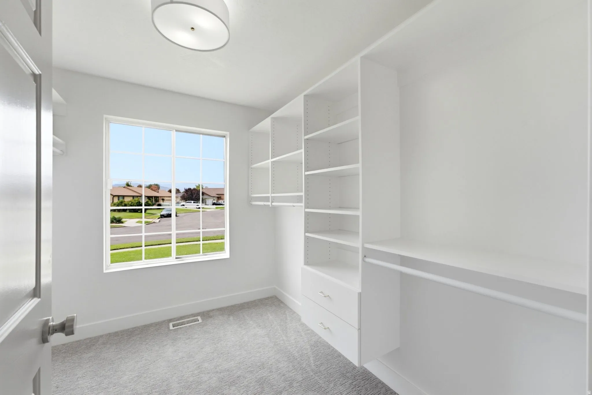 White built-in shelving with integrated drawers, hanging rods, and an overhead drum light fixture