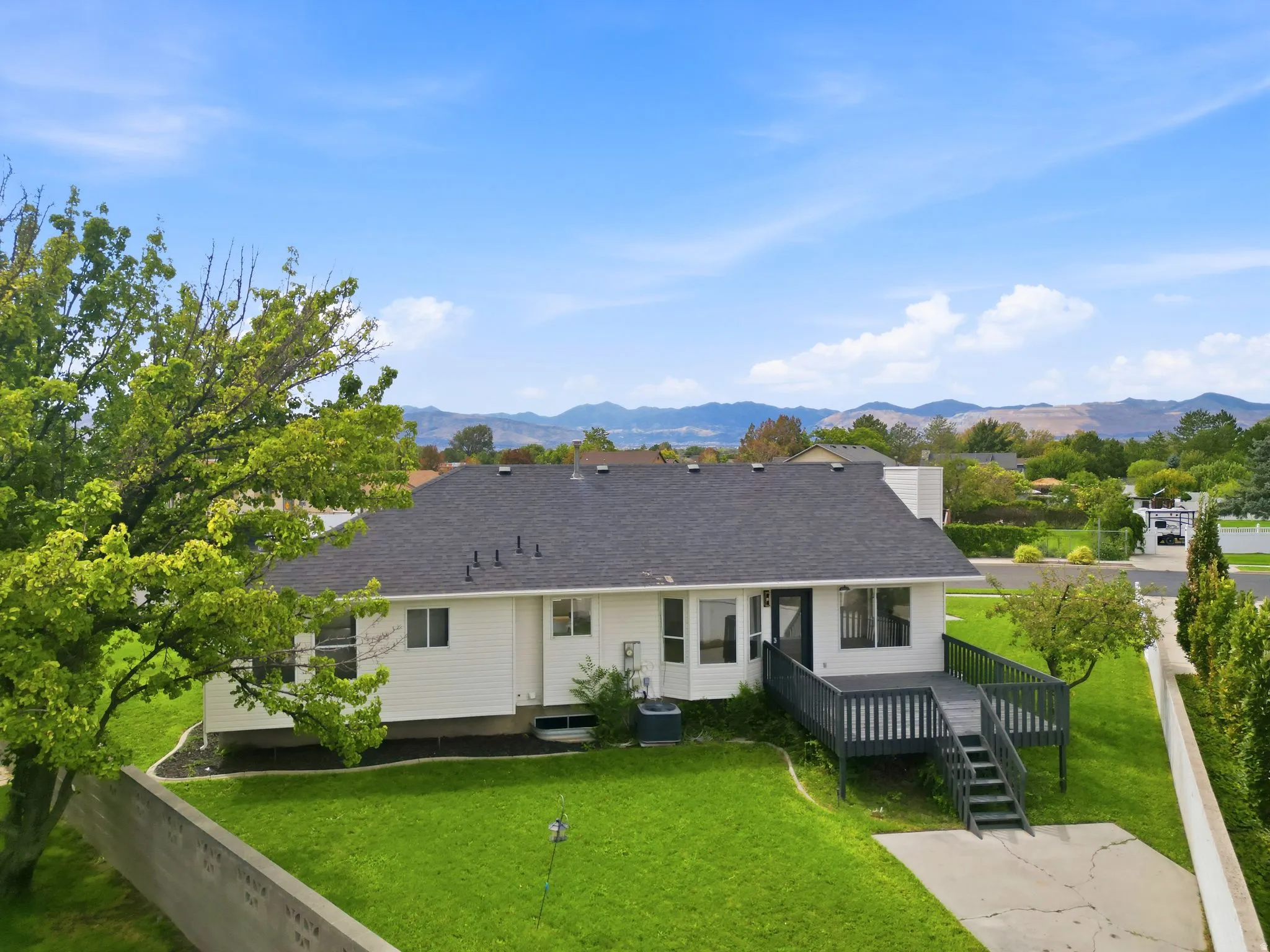 White siding exterior with dark grey roof, expansive green lawn, and a multi-level deck with stairs