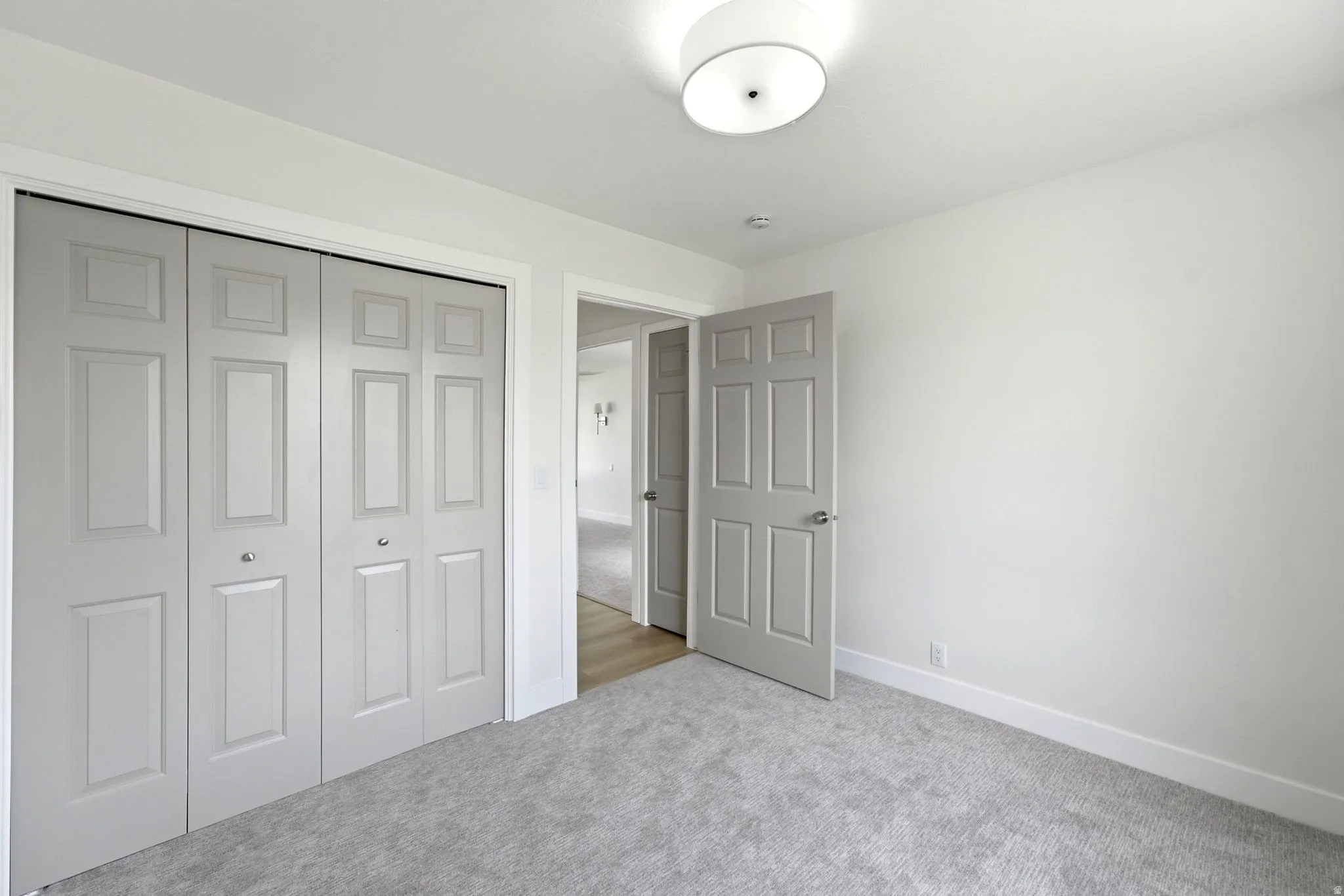 Carpeted flooring, paneled bifold closet doors, six-panel interior door, flush-mount ceiling light fixture, and white wall paint