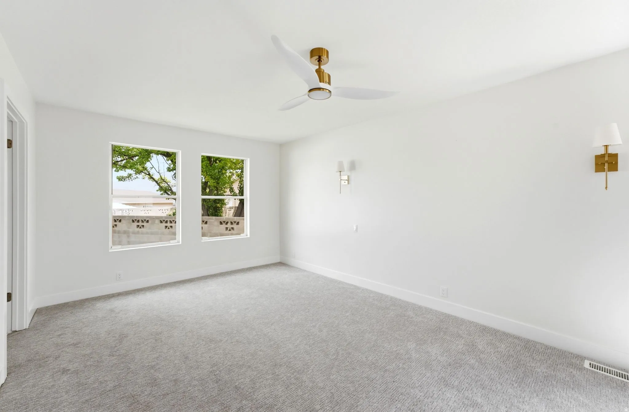 Recessed lighting, ceiling fan with gold-tone accents, two windows, carpeted flooring, and wall-mounted sconces