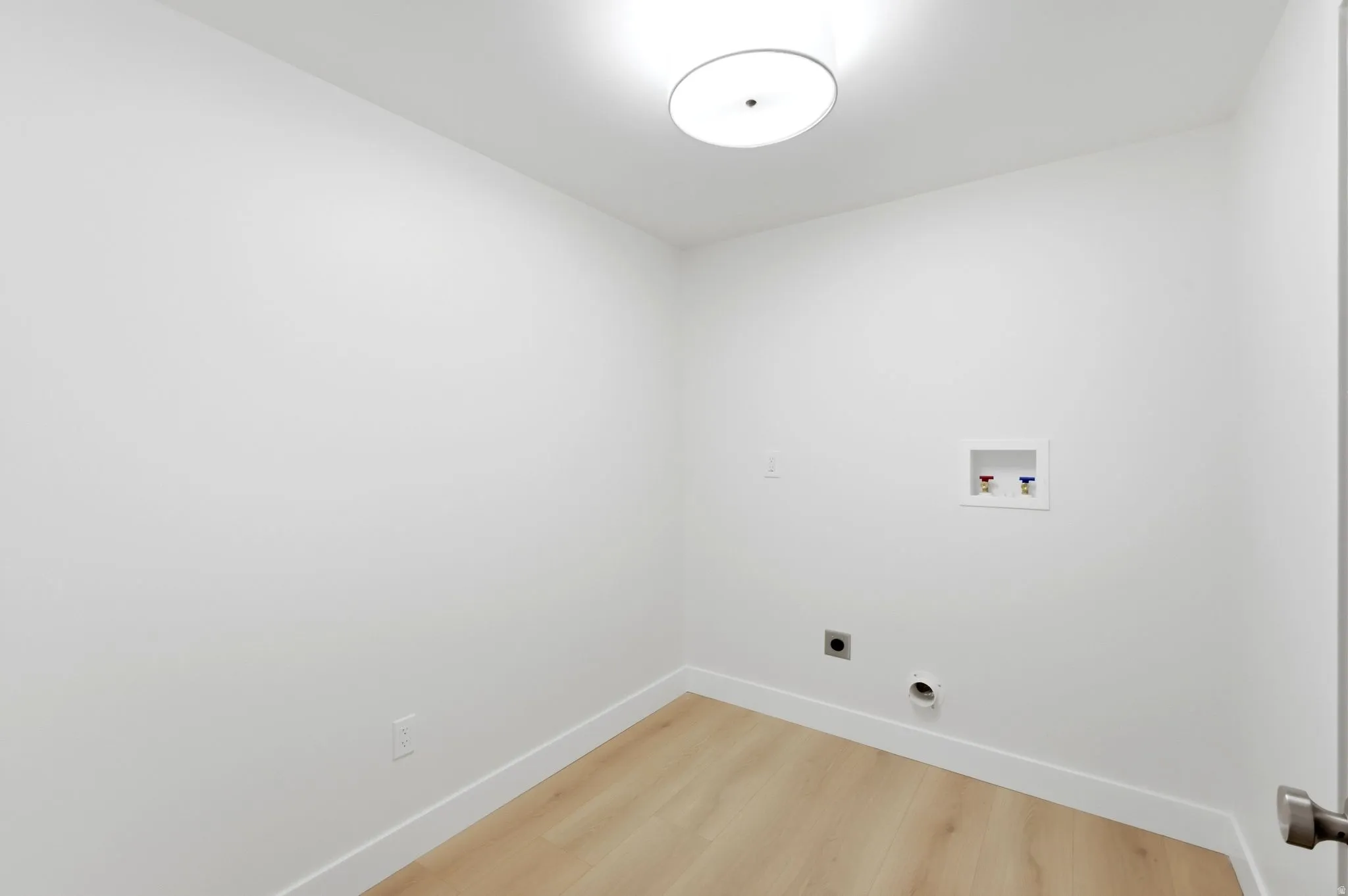 Recessed wall box for plumbing connections, light wood-finish flooring, and a flush-mount ceiling light