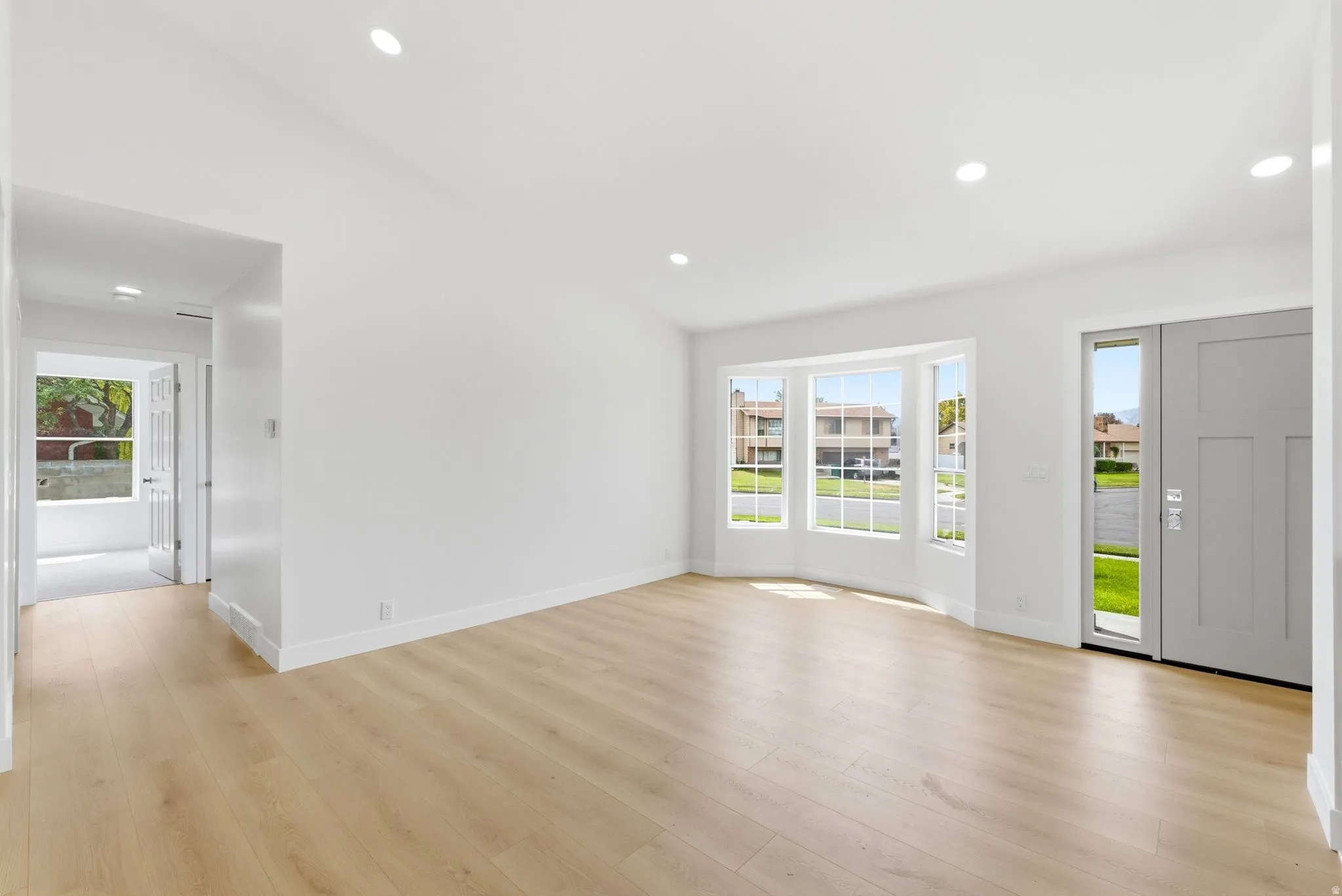 Recessed lighting illuminates the open living space, featuring wood-finish flooring and a bay window