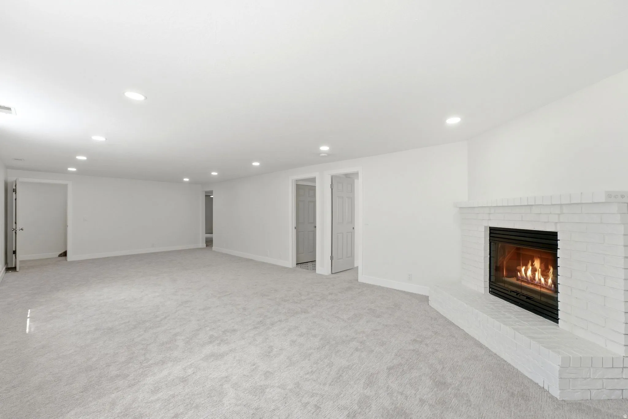 Spacious room featuring light-colored carpeting, recessed lighting, and a white brick fireplace