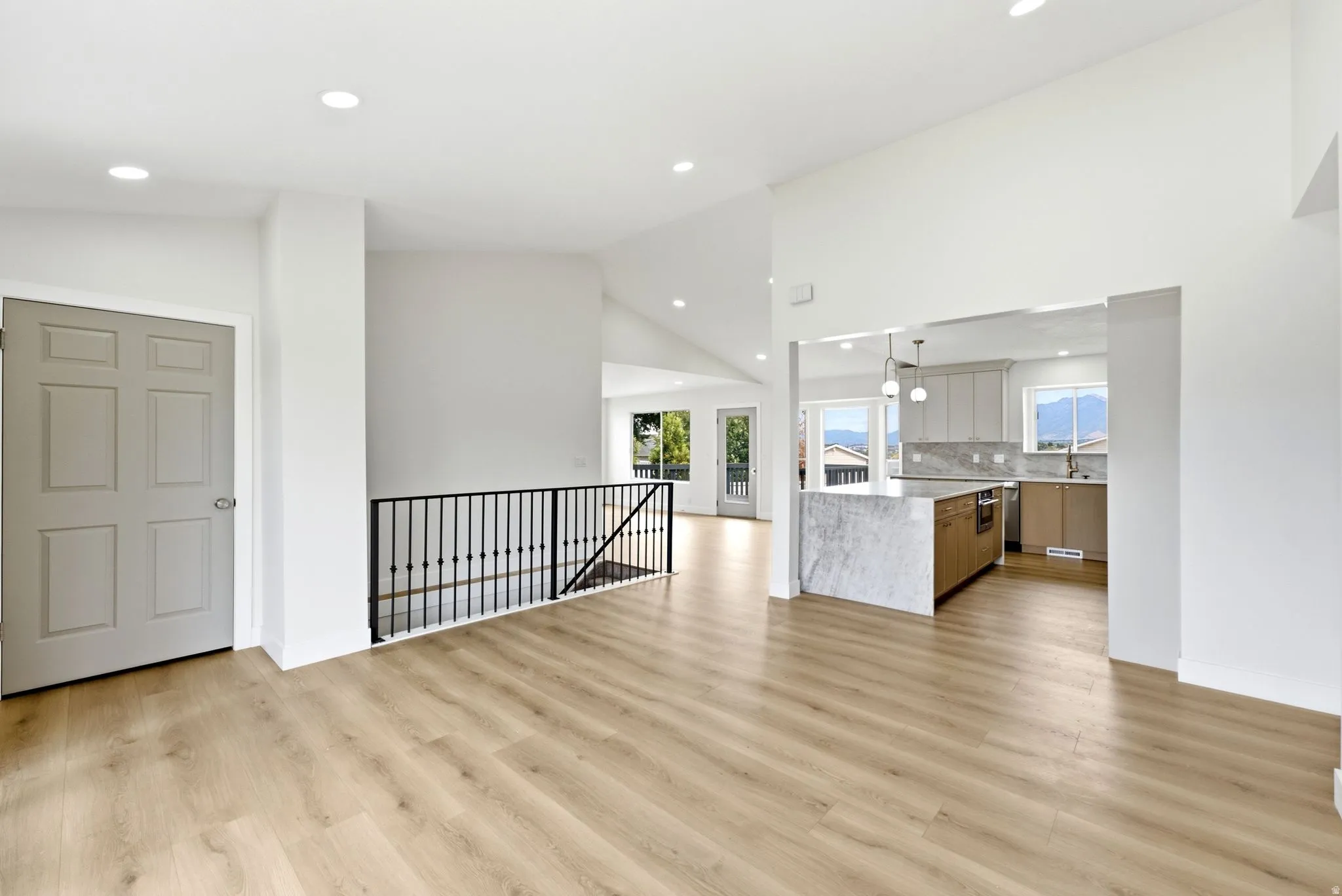 Vaulted ceiling, recessed lighting, wood-finish flooring, wrought iron railing, and a kitchen featuring a waterfall island