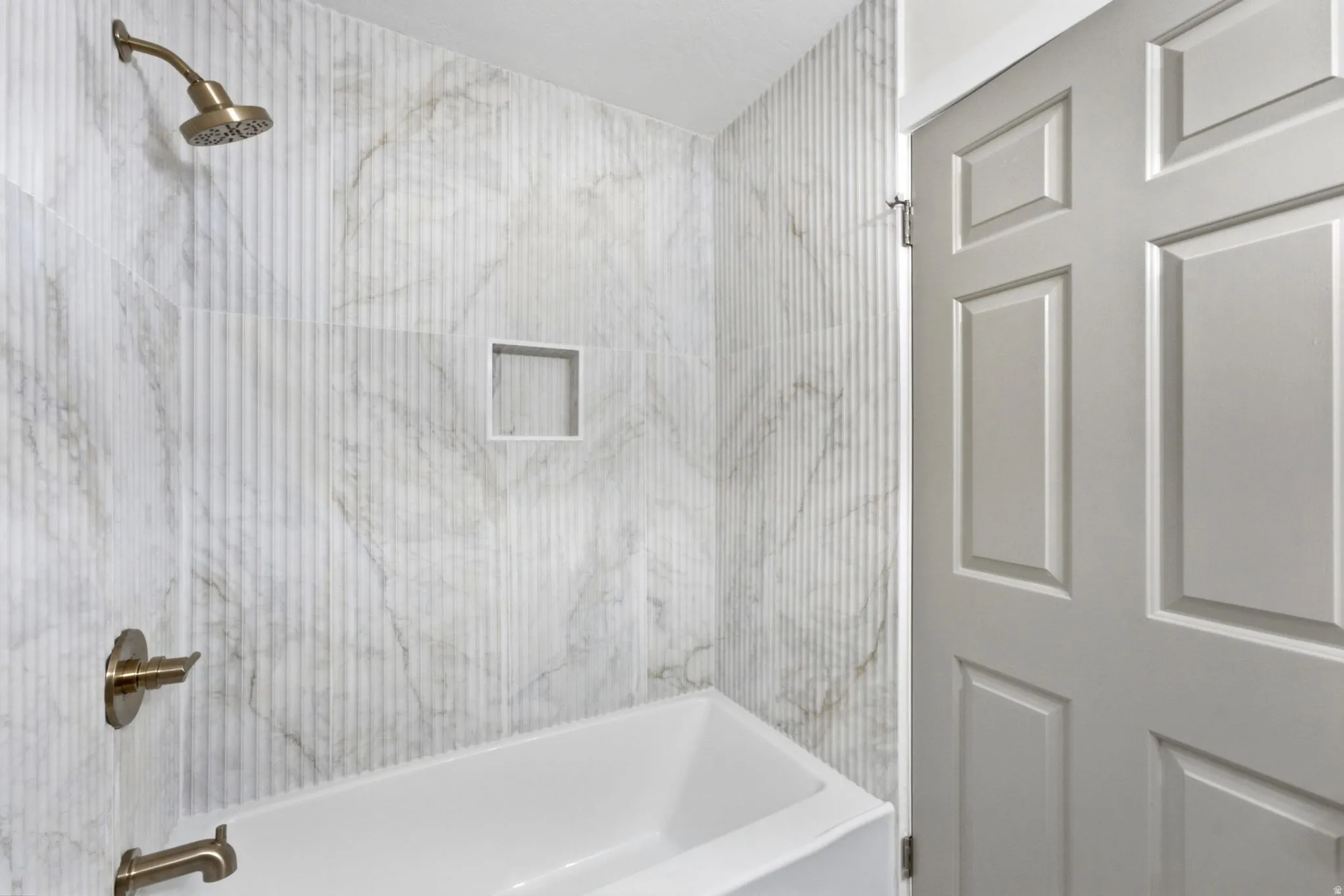 Bathtub with vertical-ribbed tile surround, integrated shower niche, and bronze fixtures