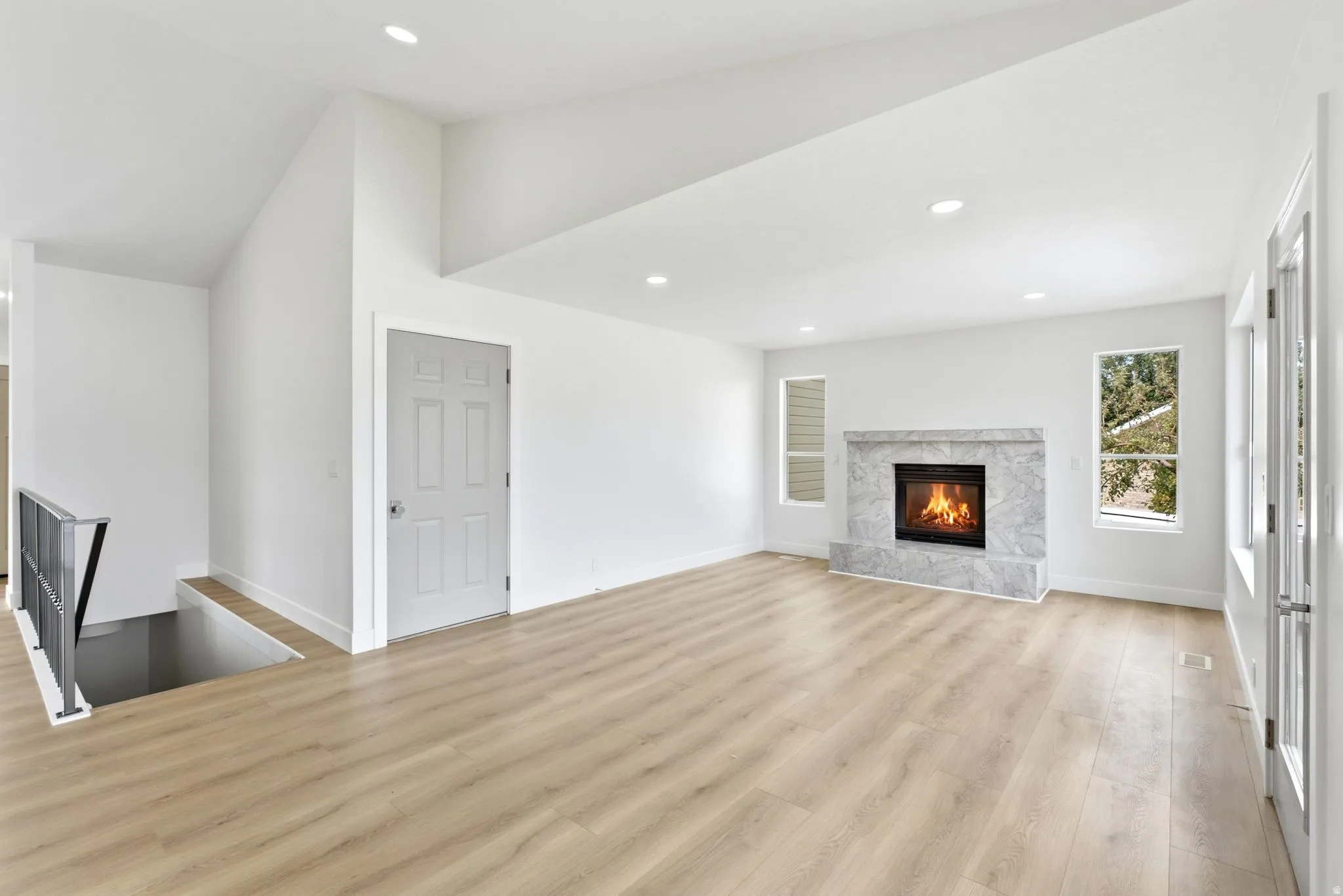 Recessed lighting, wood-finish flooring, a stone-clad fireplace, and multiple windows