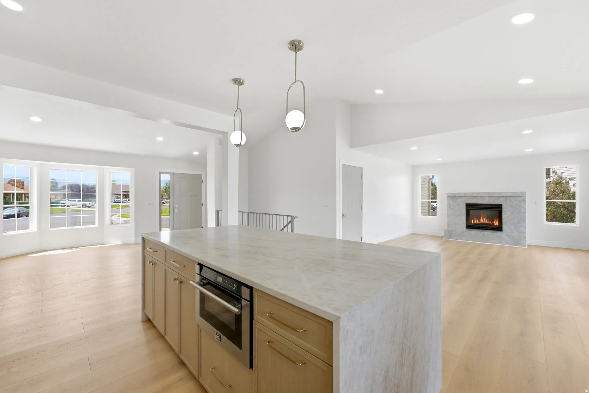 Kitchen island with integrated oven, light wood-finish flooring, vaulted ceilings, recessed lighting, and a fireplace with a stone surround