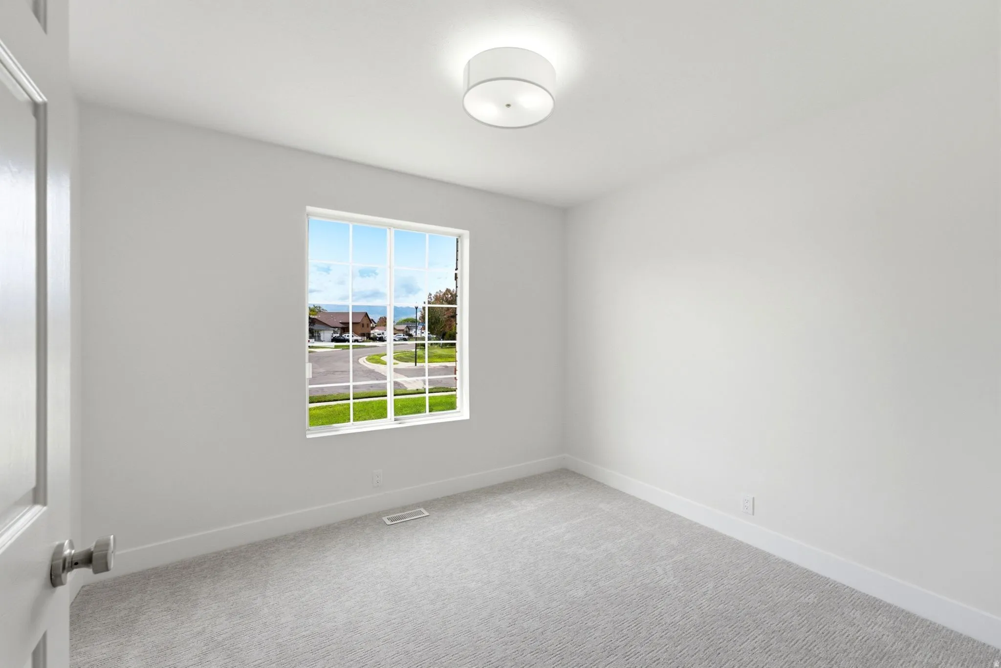 Neutral wall color, window with grid panes, textured carpet flooring, flush mount ceiling light fixture, white interior door