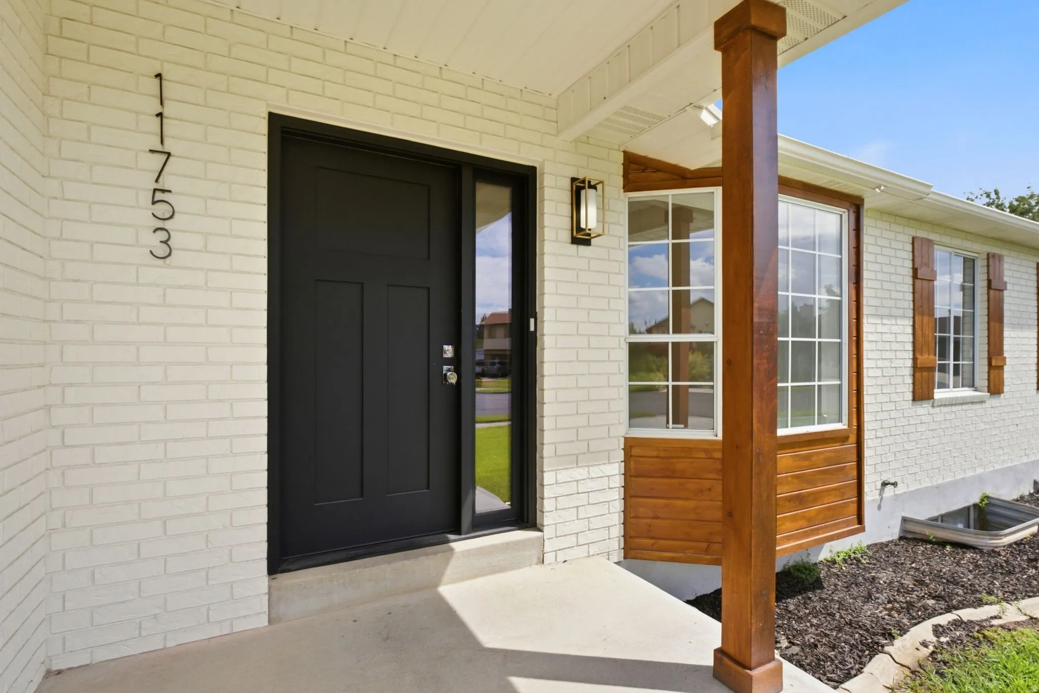 White brick exterior with a dark-paneled entry door, a sidelight, and an exterior sconce
