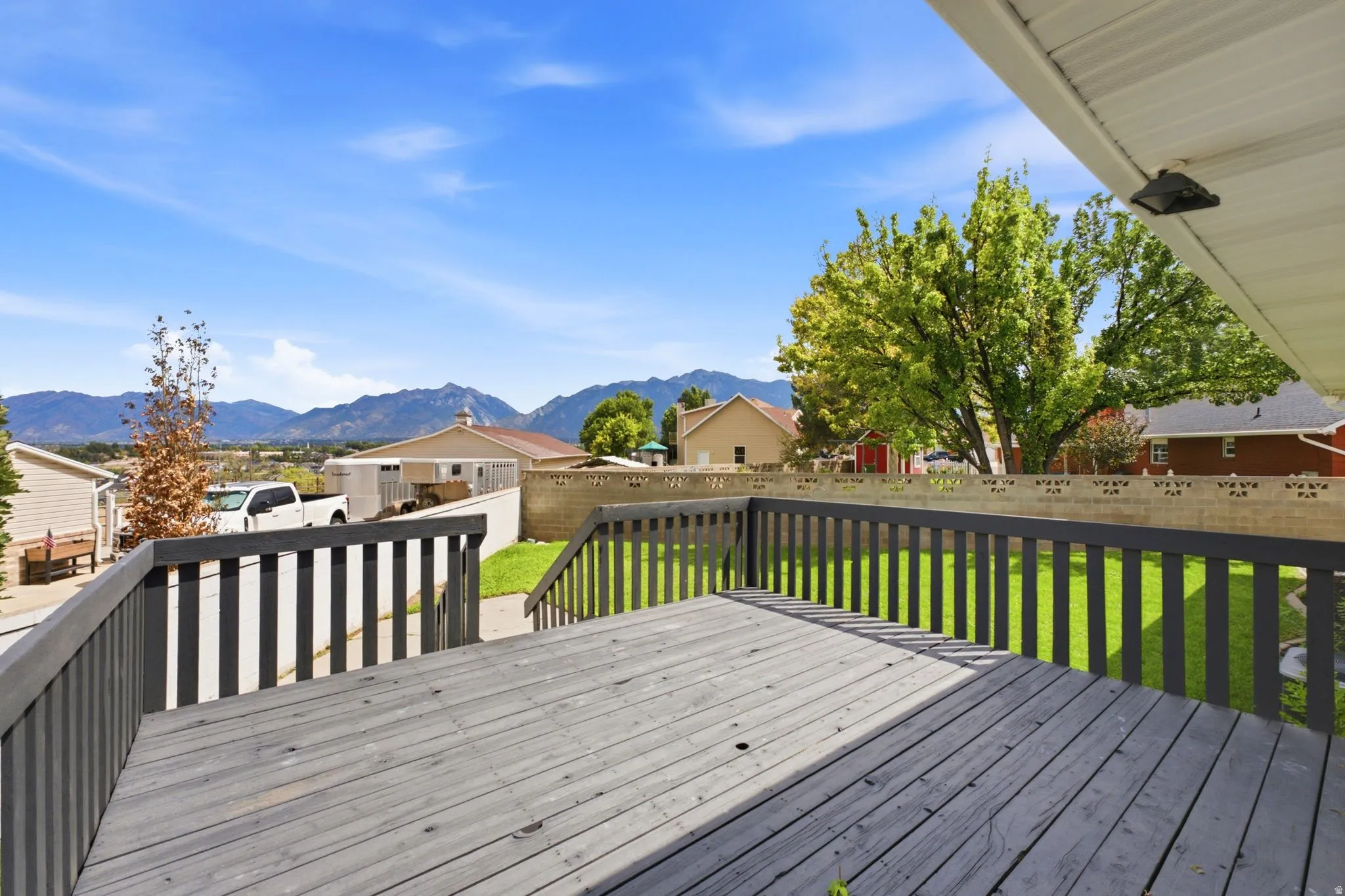 Expansive exterior deck with dark railings, a lush green lawn, and a distant mountain backdrop under a clear sky