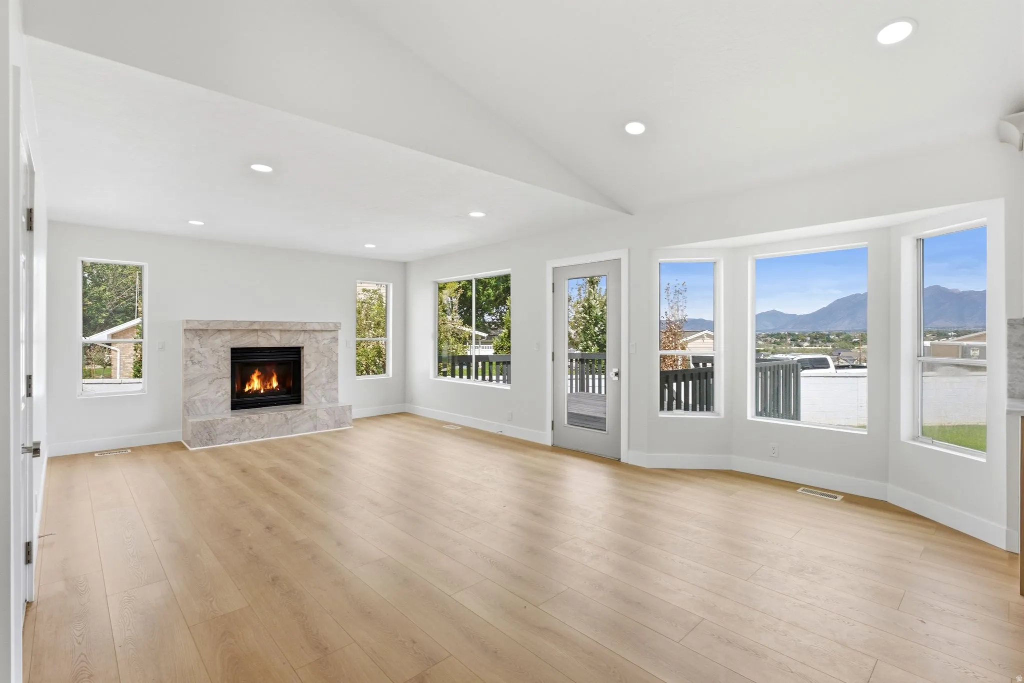 Vaulted ceilings, a fireplace with a stone surround, wood-finish flooring, recessed lighting, and expansive windows