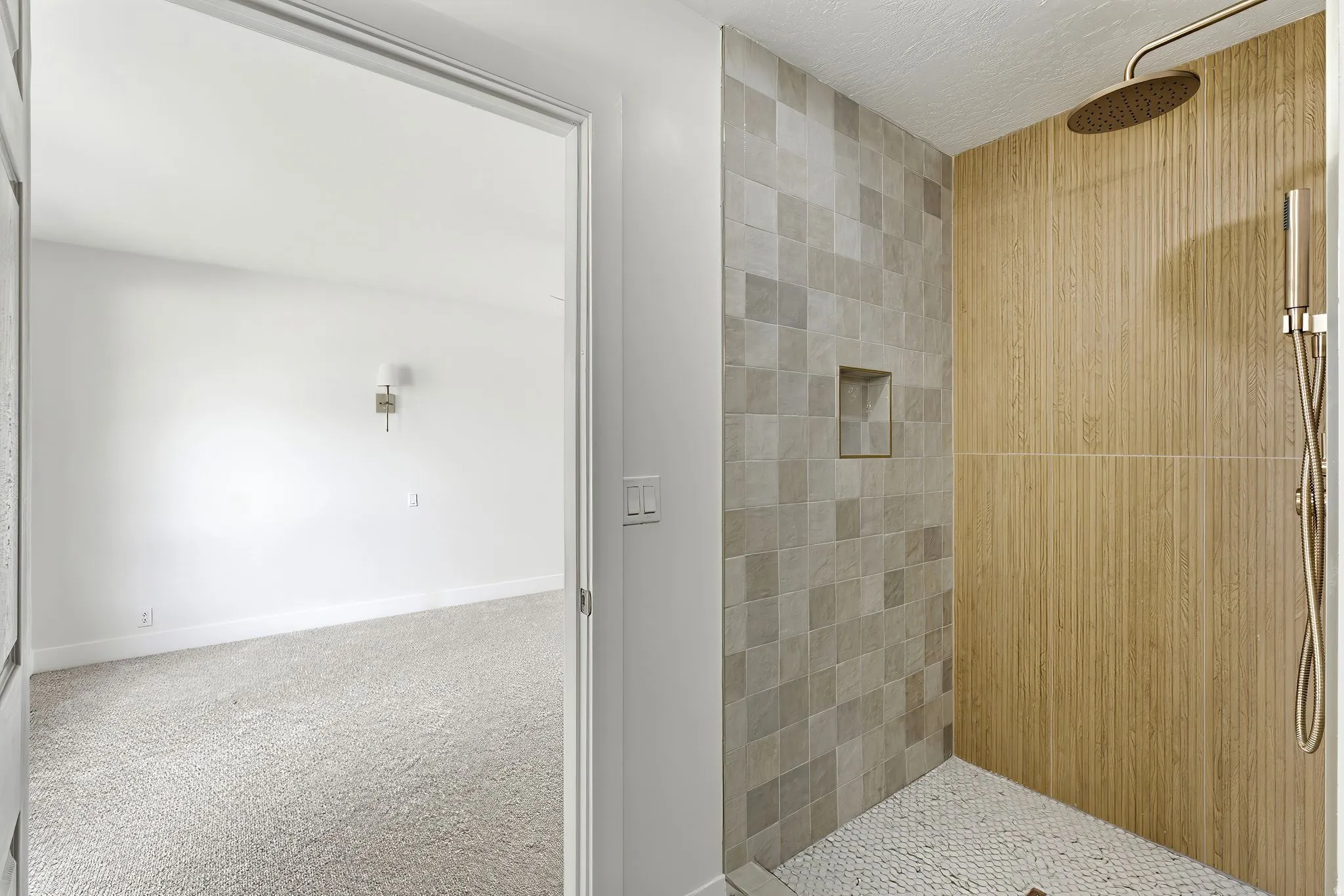 Shower featuring dual-textured tile walls, recessed shelf, pebble flooring, and a rainfall showerhead with an additional handheld spray
