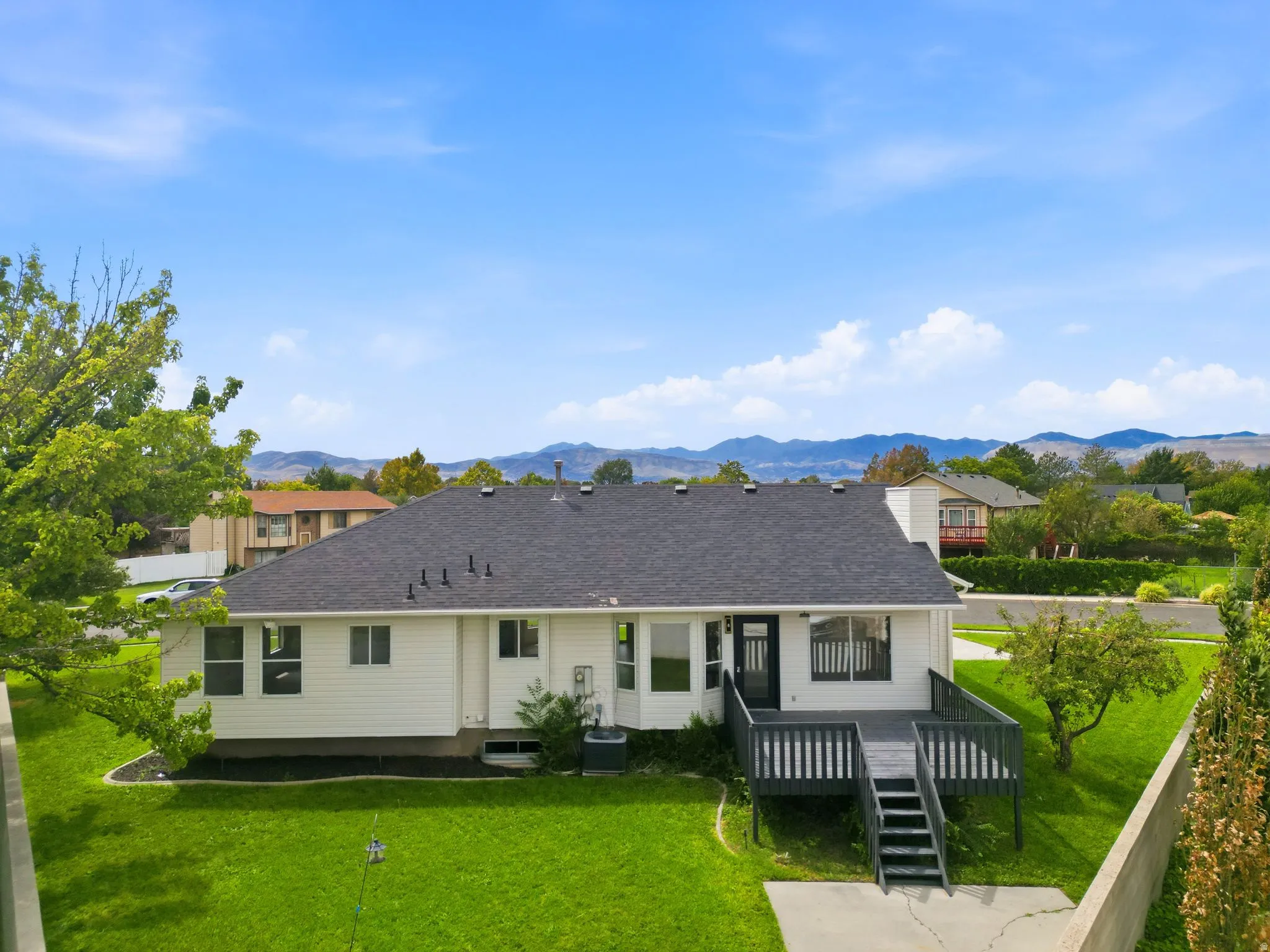 Expansive backyard featuring a manicured lawn, a multi-level deck with steps, and distant mountain scenery