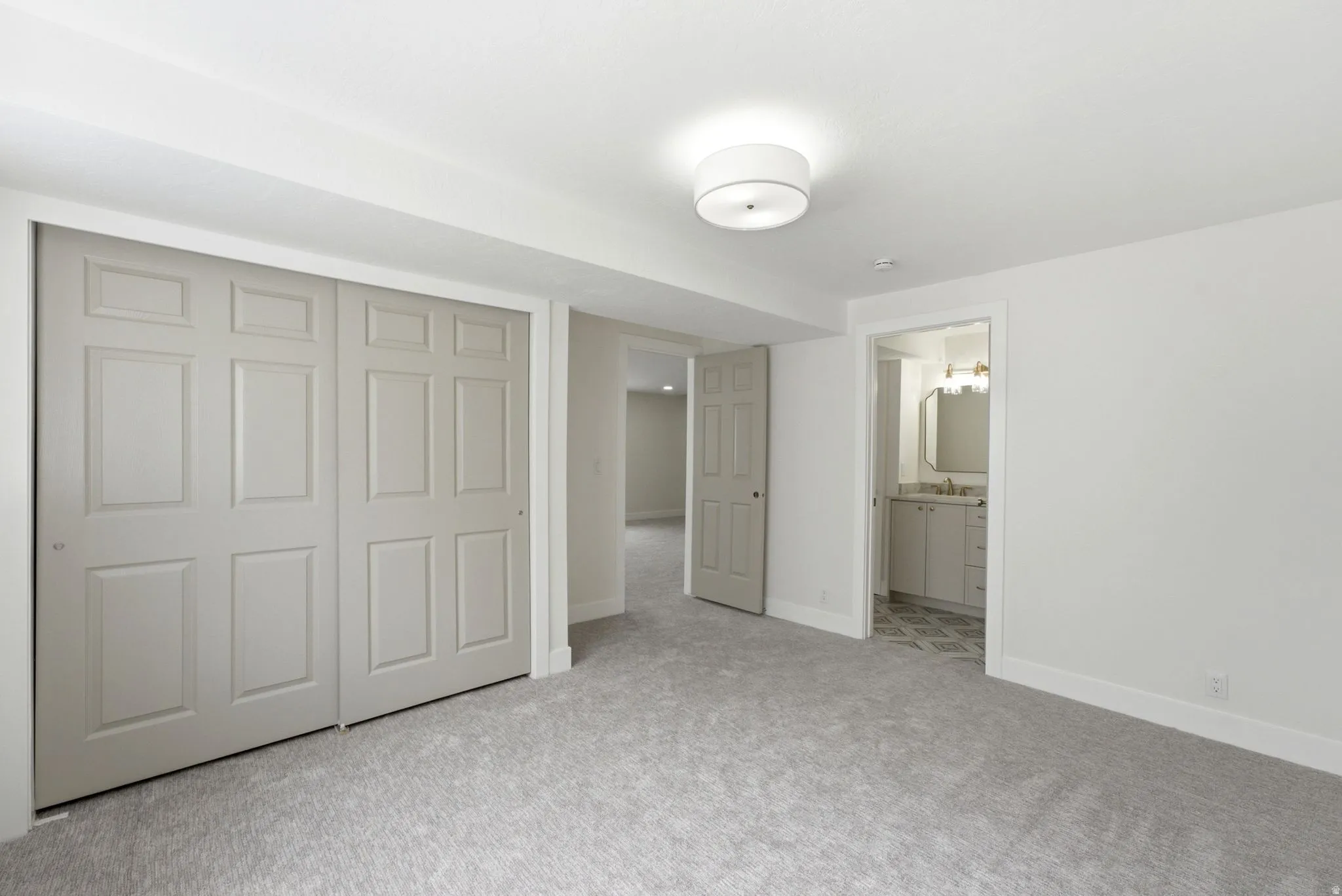 Neutral-toned paneled closet doors, soft gray carpeting, recessed ceiling, flush mount ceiling light fixture, and a white vanity with a rectangular sink