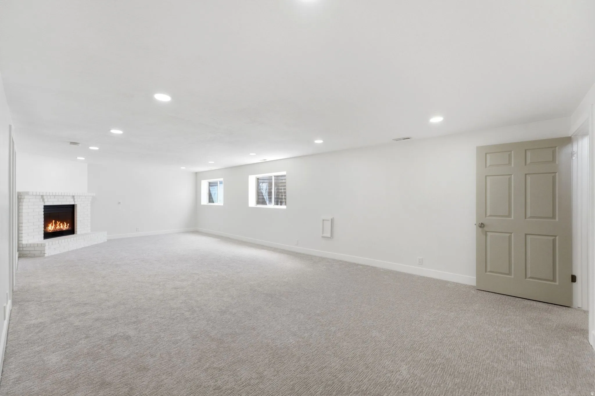Expansive room with neutral carpet, recessed lighting, and a white brick fireplace