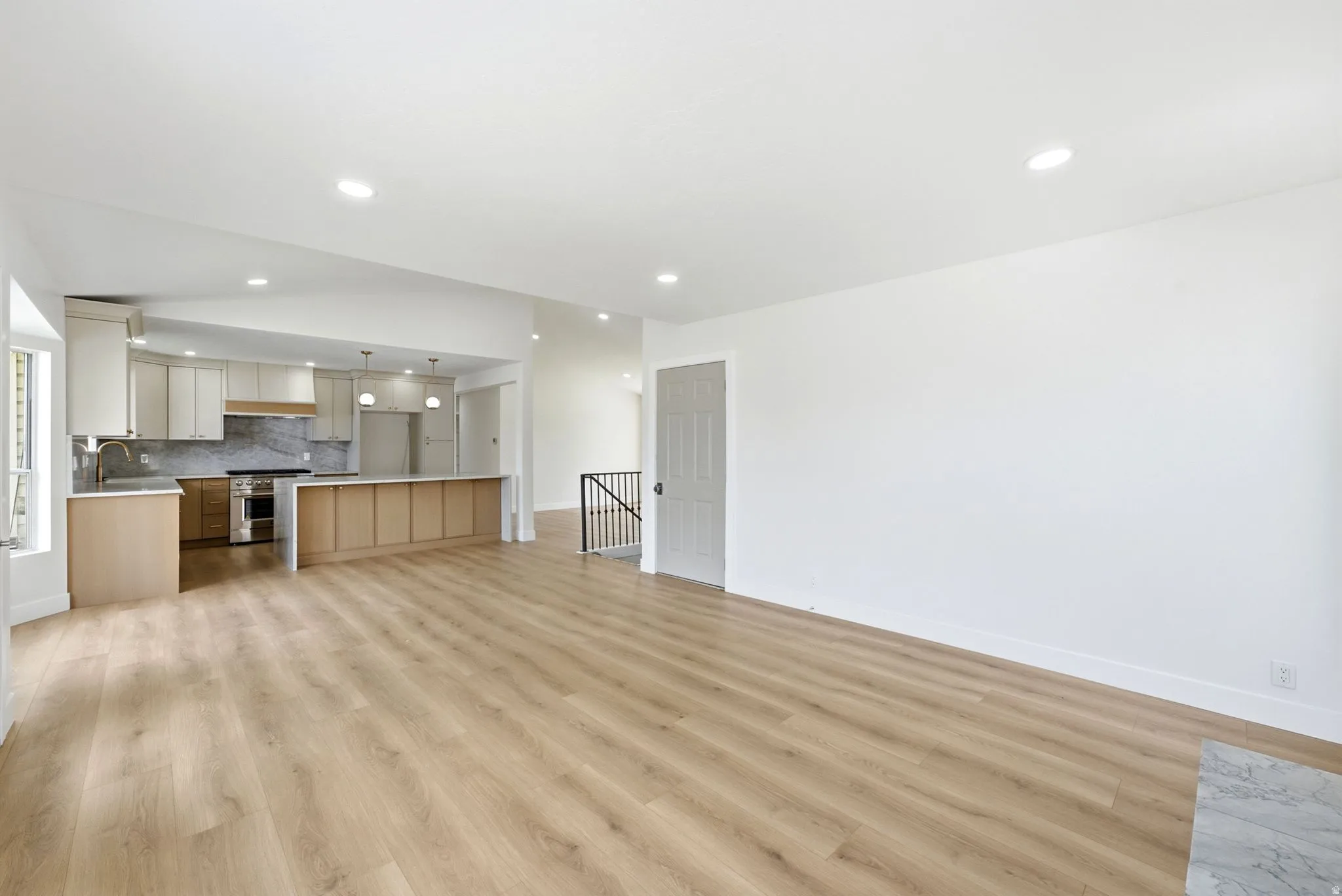 Open-concept living space with wood-finish flooring, recessed lighting, and a kitchen featuring a peninsula with integrated cabinetry, stainless steel appliances, and a full-height backsplash