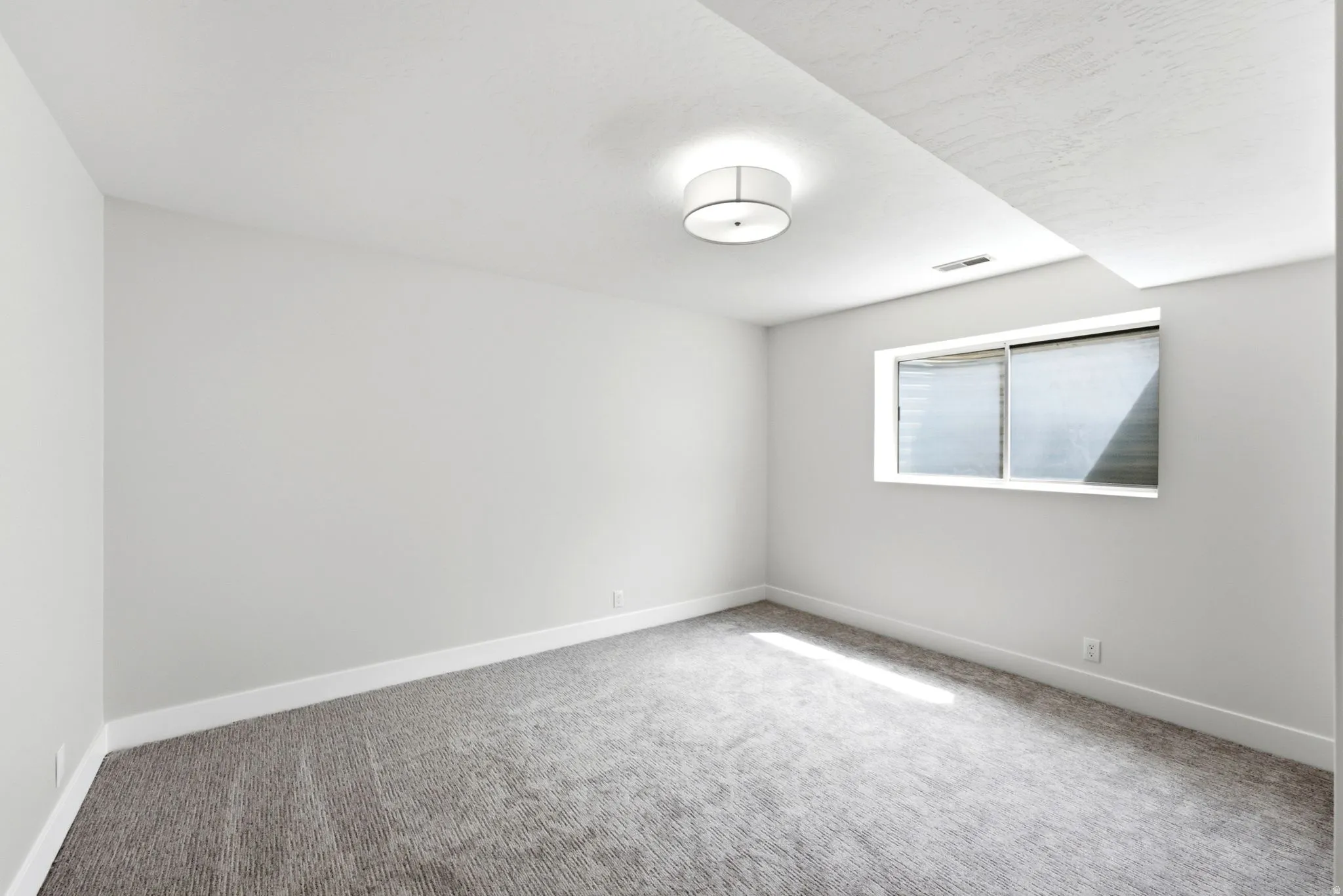 Neutral wall paint, gray carpeting, a single window, and a ceiling-mounted light fixture