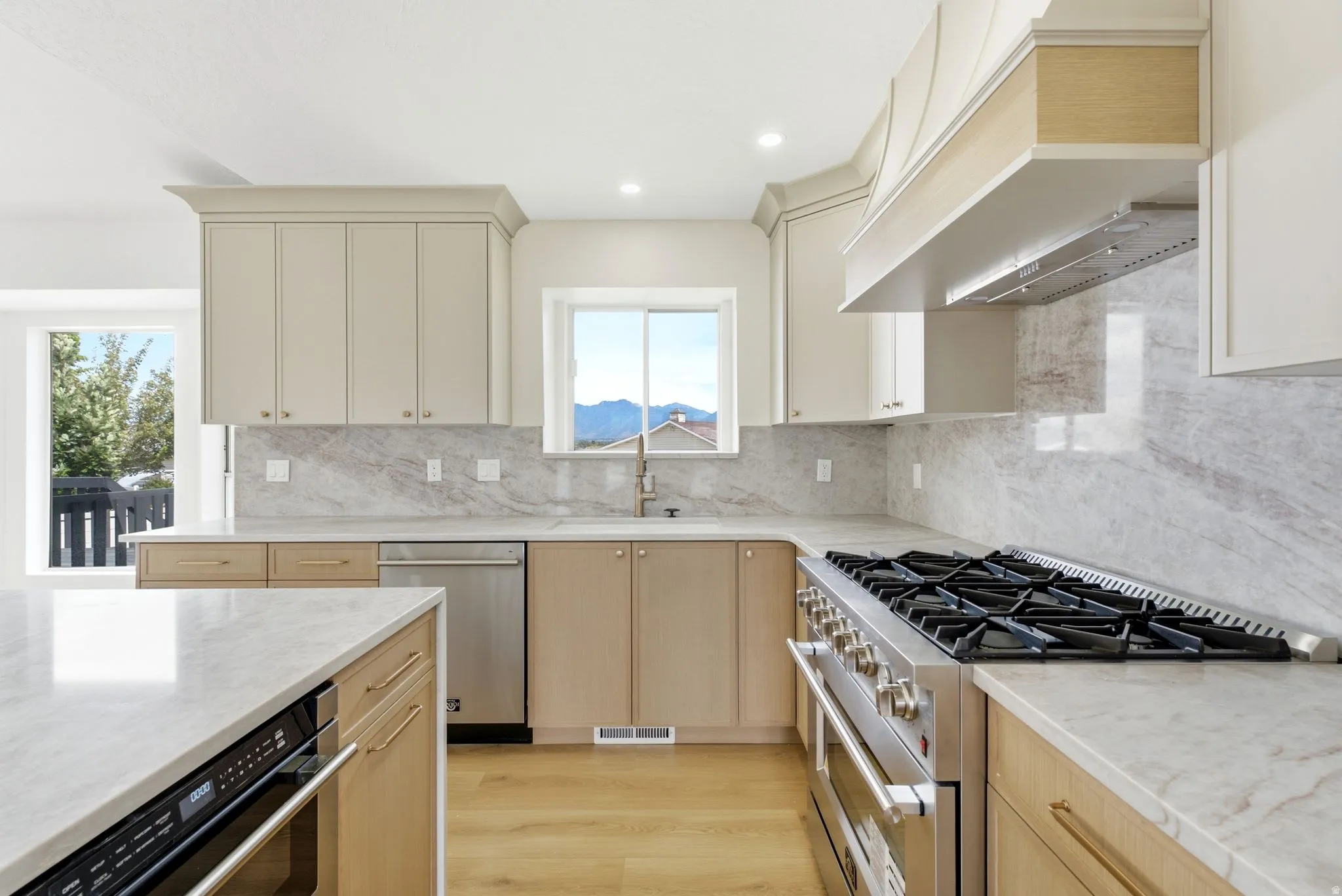Gourmet kitchen featuring a professional-grade range, integrated stainless steel appliances, solid surface countertops, light wood-finish flooring, and a decorative range hood