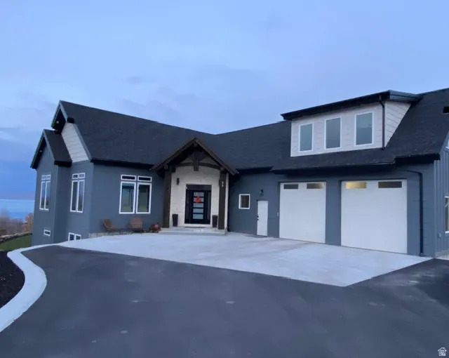 Modern exterior with dark siding, stone accents, a multi-pane front entry door, a two-car garage, and an asphalt driveway