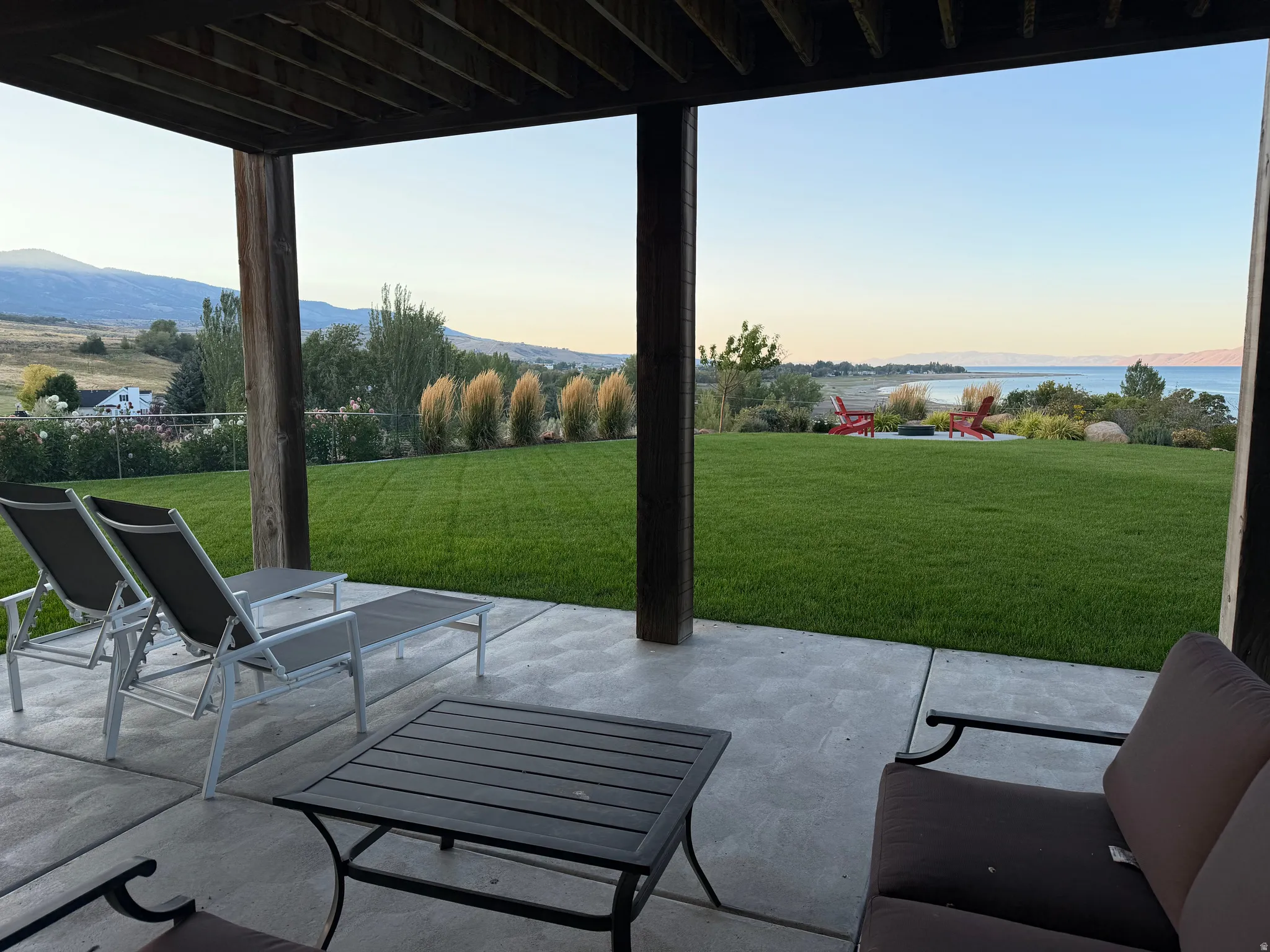 Covered patio with concrete surface, expansive lawn, distant water body, and mountain backdrop