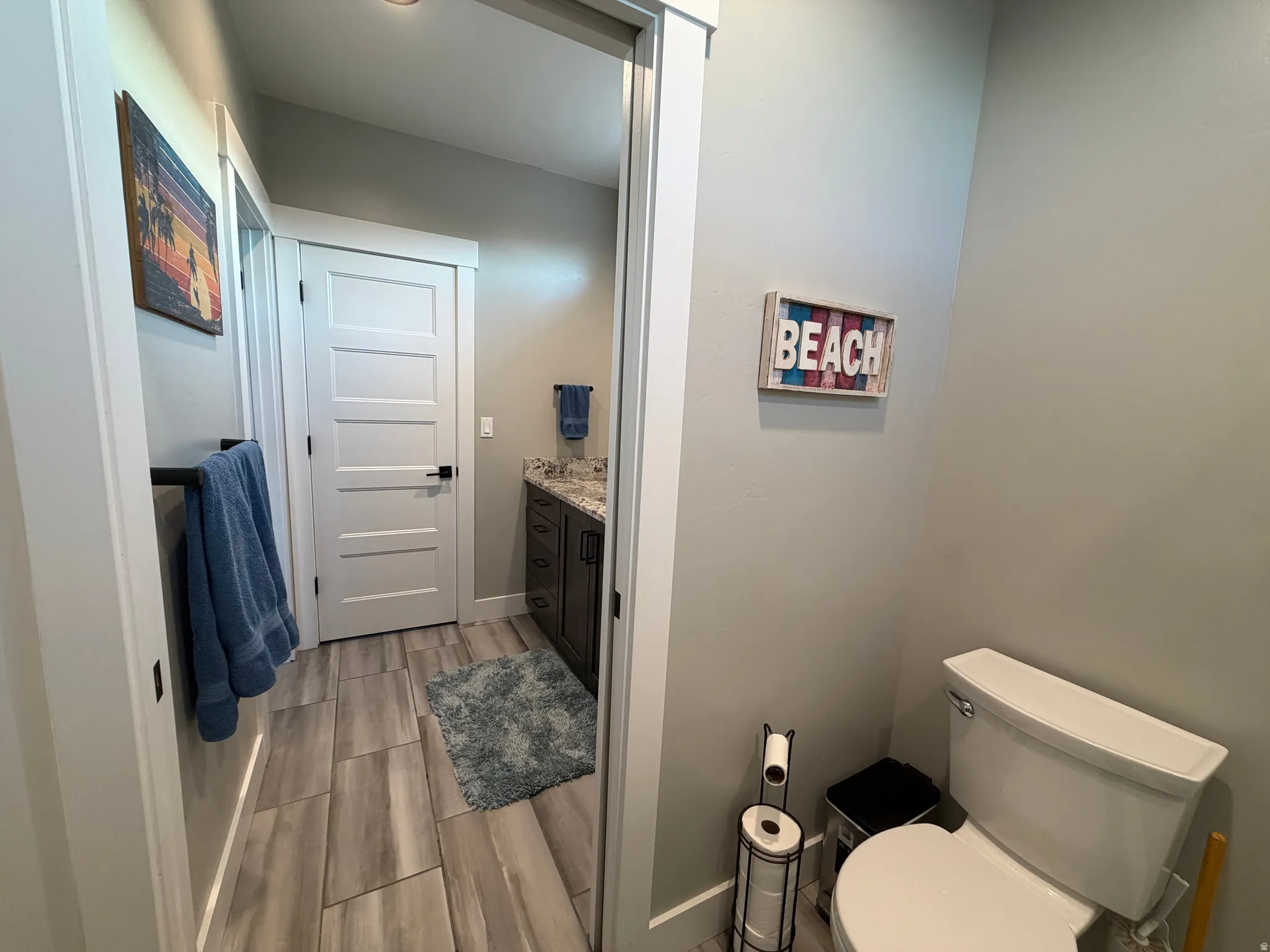 Bathroom featuring wood-finish tile flooring, a dark wood-finish vanity with a light-toned countertop, and a white toilet