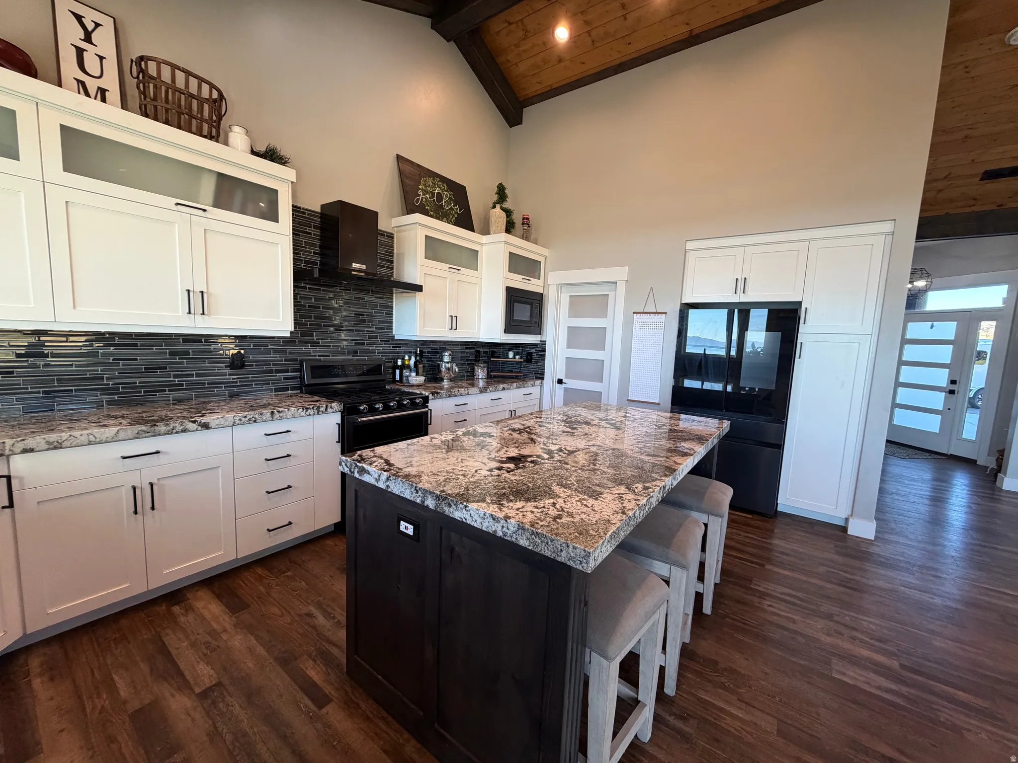 Vaulted wood-finish ceiling, white cabinetry with dark hardware, stone countertops, dark tile backsplash, and wood-finish flooring