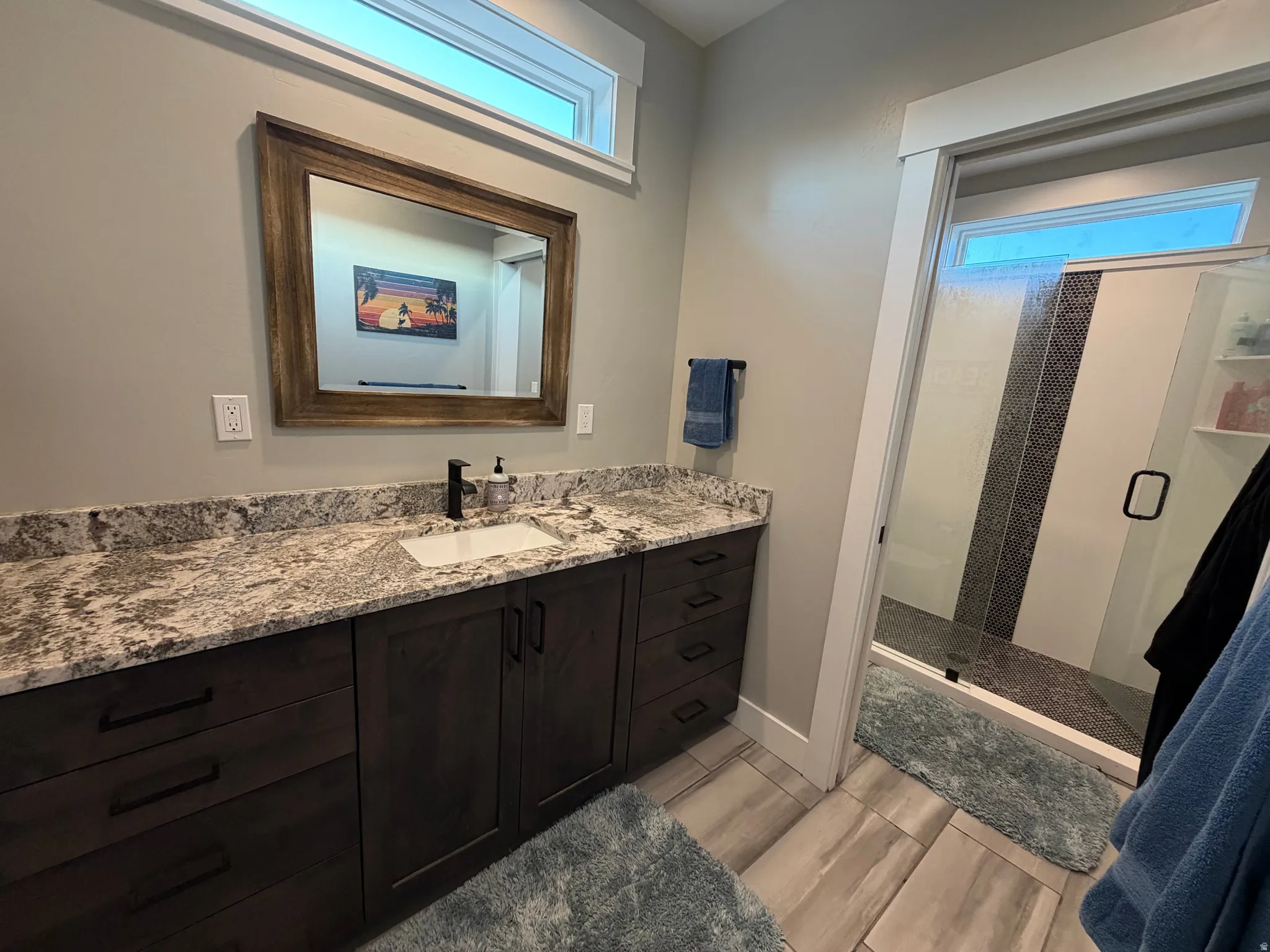 Spacious vanity with a granite countertop, undermount sink, dark wood-finish cabinetry, and matte black fixtures