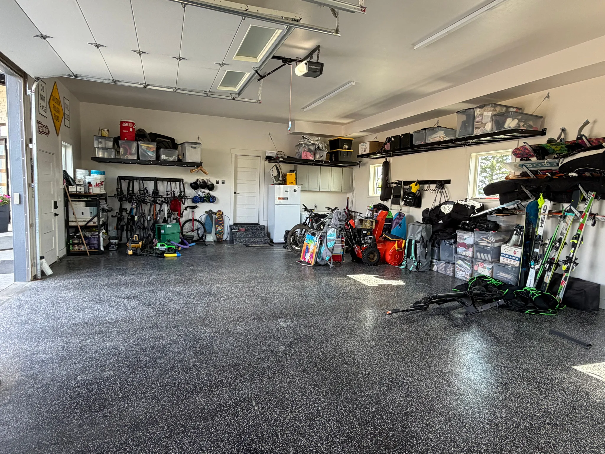 Spacious garage featuring a durable speckled epoxy floor, overhead storage racks, recessed lighting, and windows for natural light