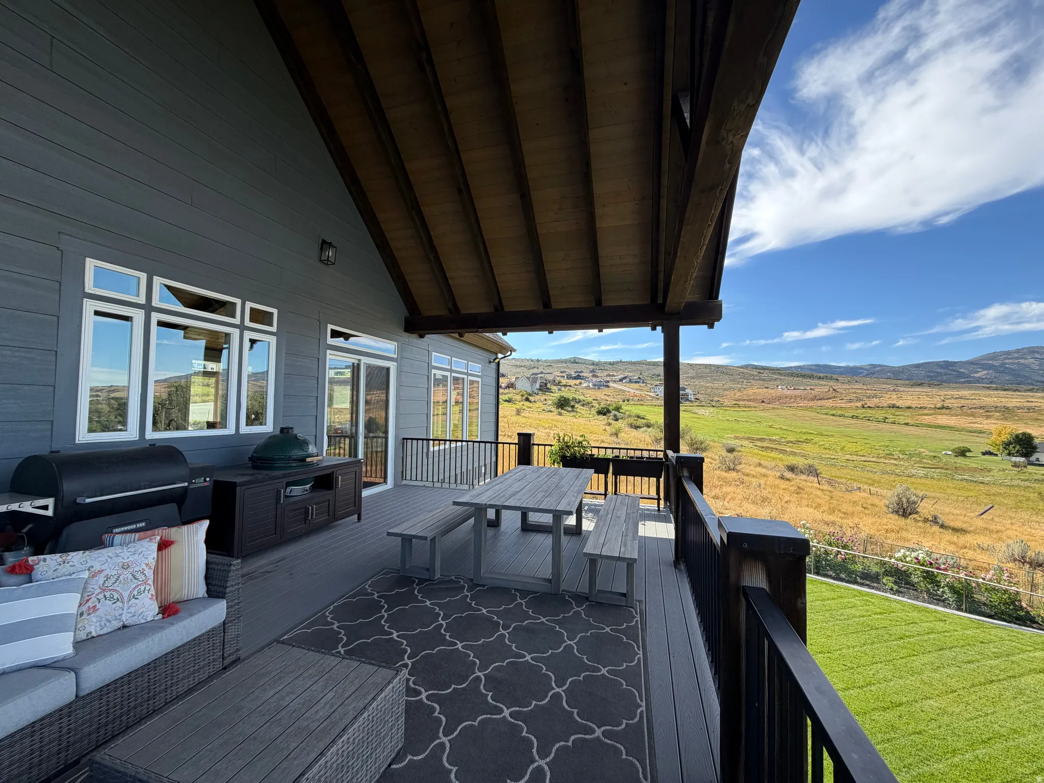 Expansive covered deck with composite decking, black metal railings, and a wood-beamed ceiling