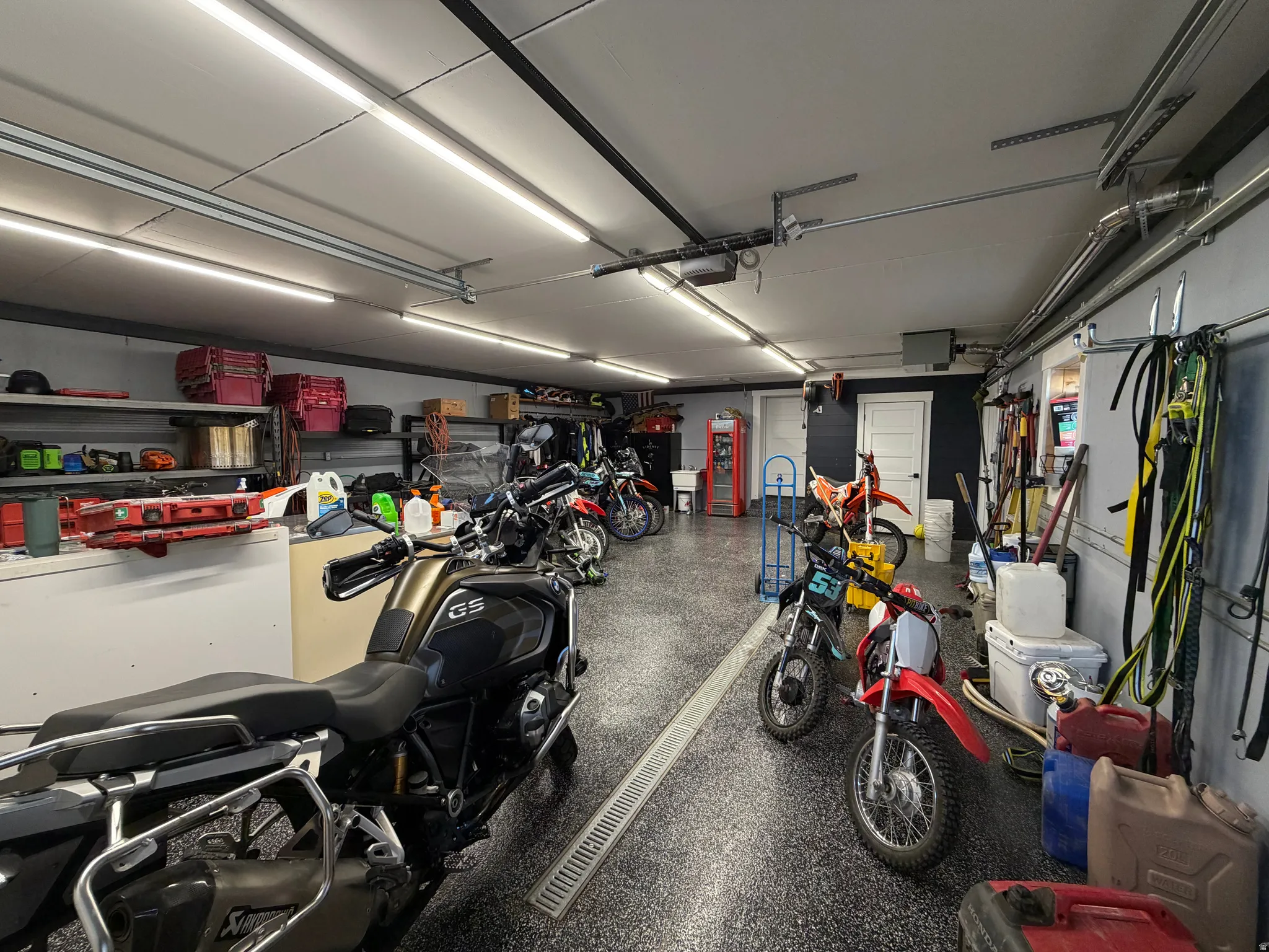 Spacious garage with epoxy flooring, multiple linear ceiling lights, integrated track lighting, and built-in shelving