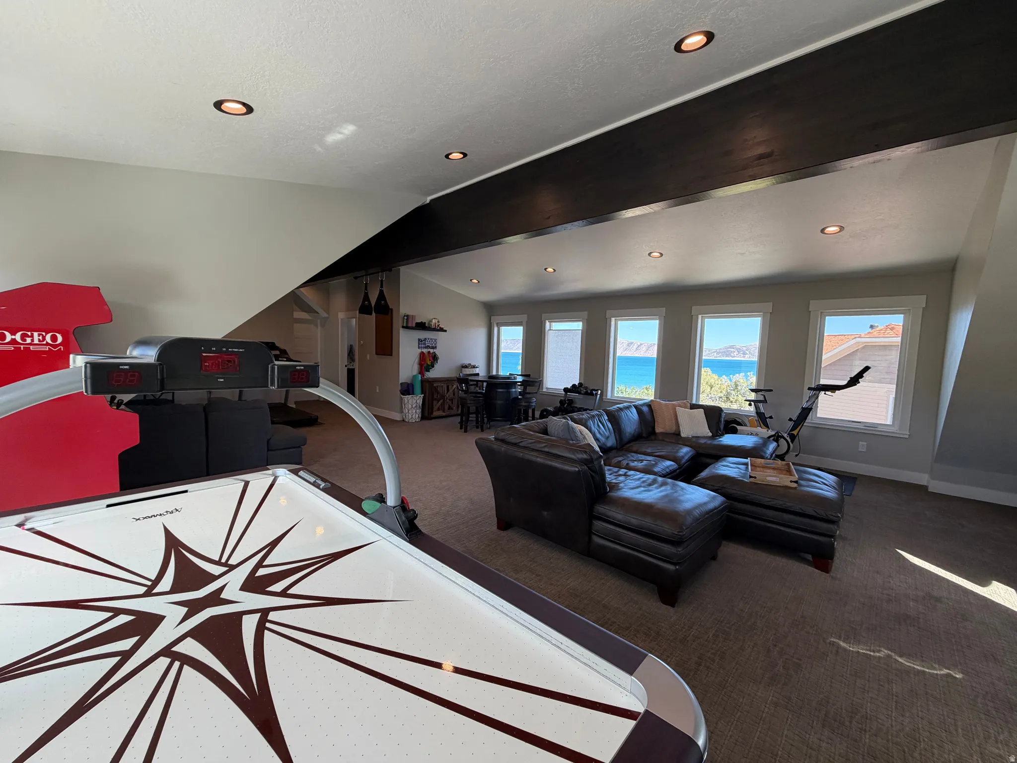 Recessed lighting illuminates this space featuring multiple windows, a prominent dark-finished ceiling beam, and a neutral carpet