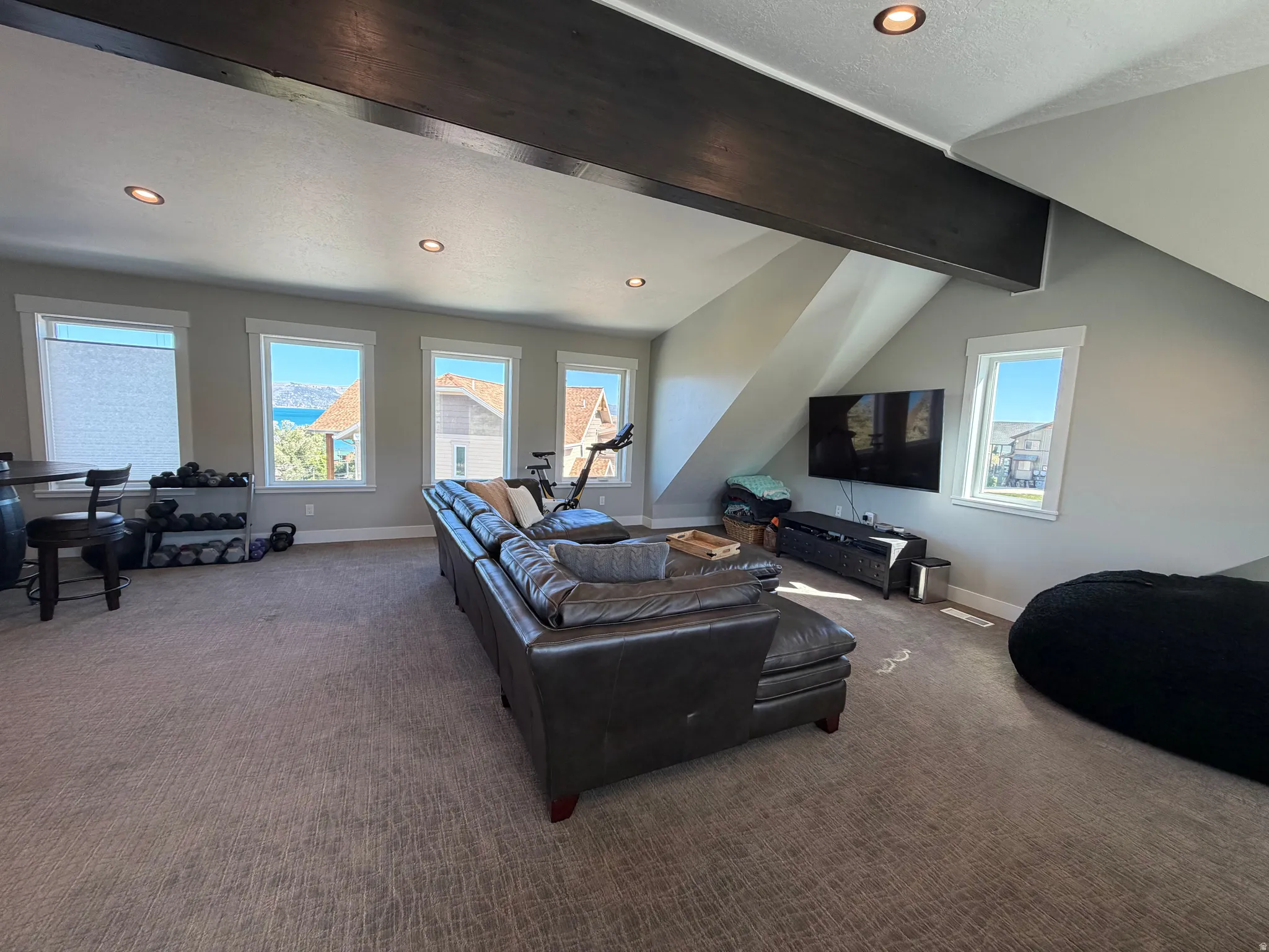 Recessed ceiling lighting, exposed structural beam, multiple windows, carpet flooring, and a partial vaulted ceiling