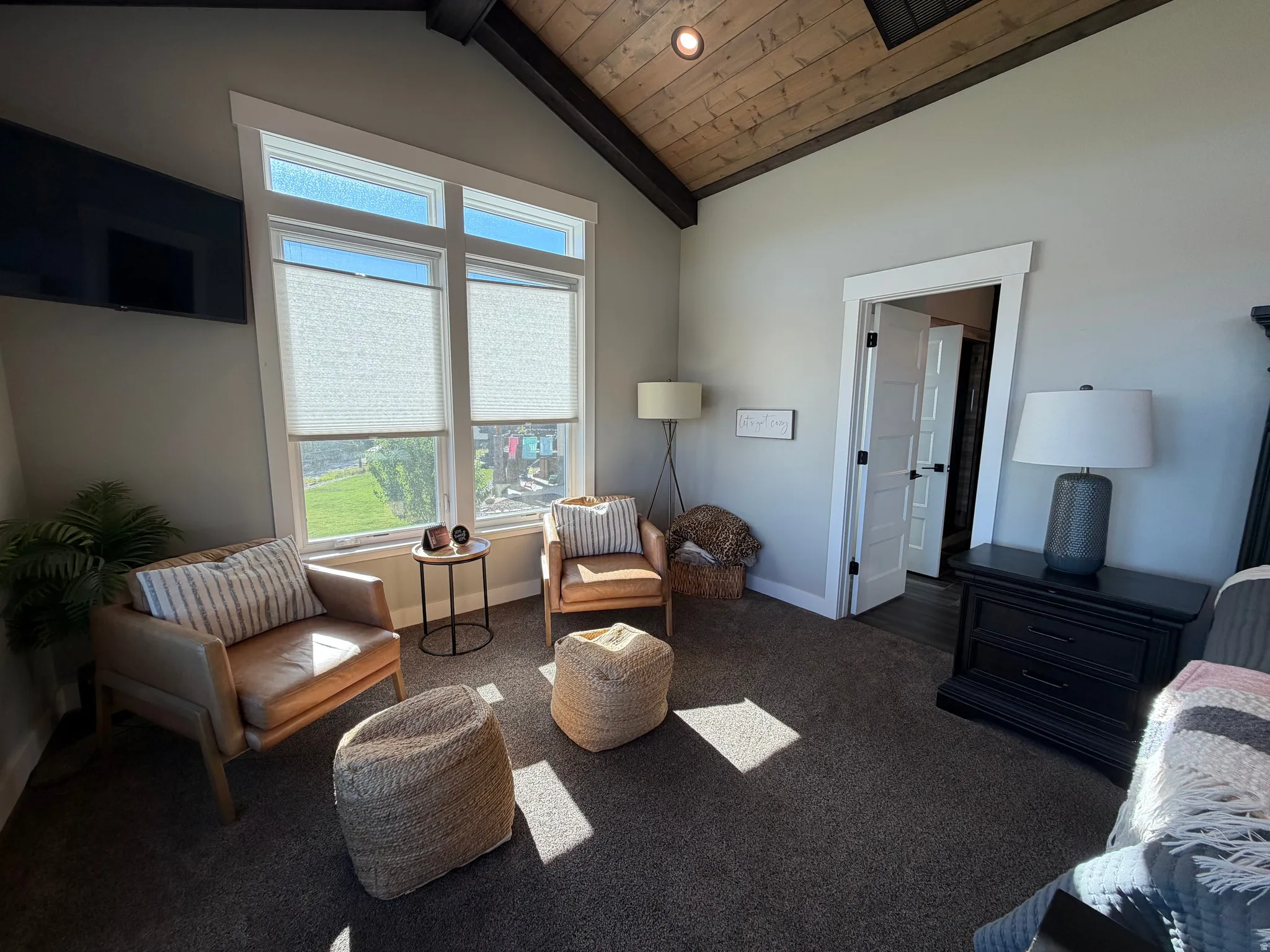 Vaulted wood-paneled ceiling with exposed beams, large windows with white trim, wall-mounted television, and a built-in closet with a paneled door