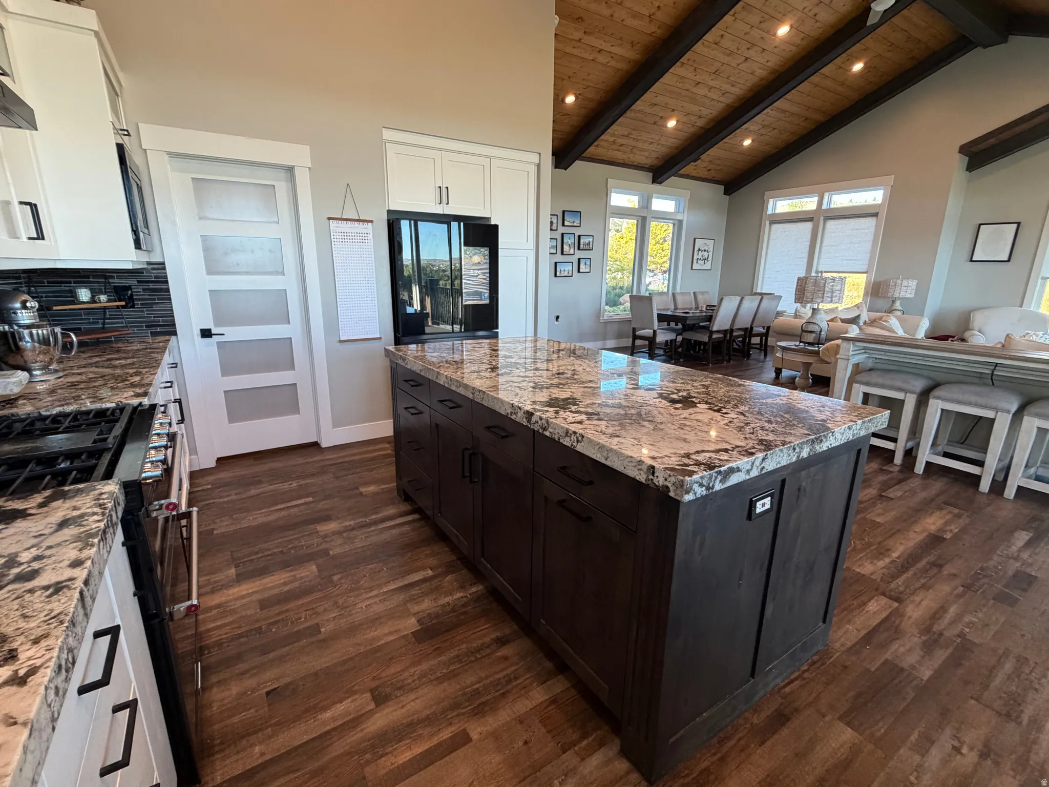 Kitchen featuring an oversized island with a stone countertop, wood-finish flooring, white cabinetry, dark subway tile backsplash, and stainless steel appliances