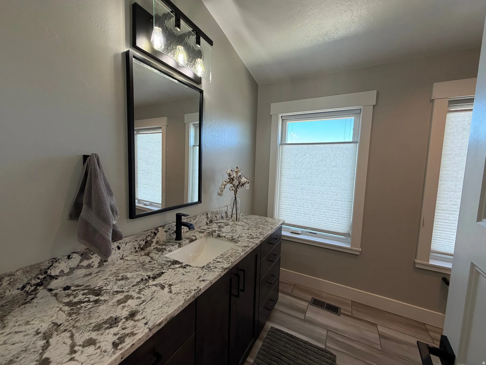 Vanity with white rectangular undermount sink, dark wood-finish cabinetry, and a patterned stone countertop
