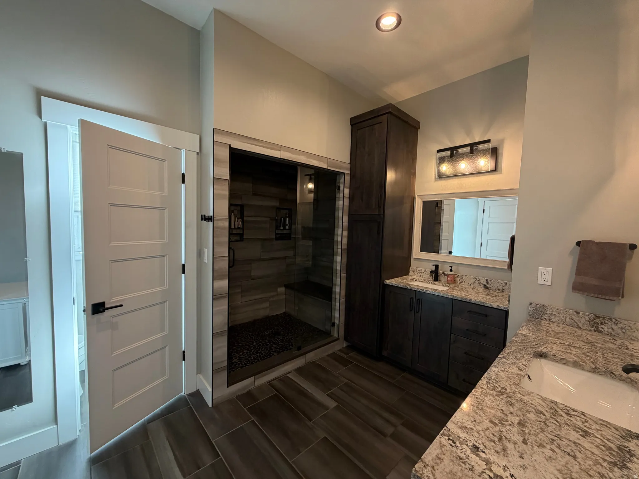 Dual vanity with stone countertops, wood-finish flooring, and a walk-in shower with glass enclosure