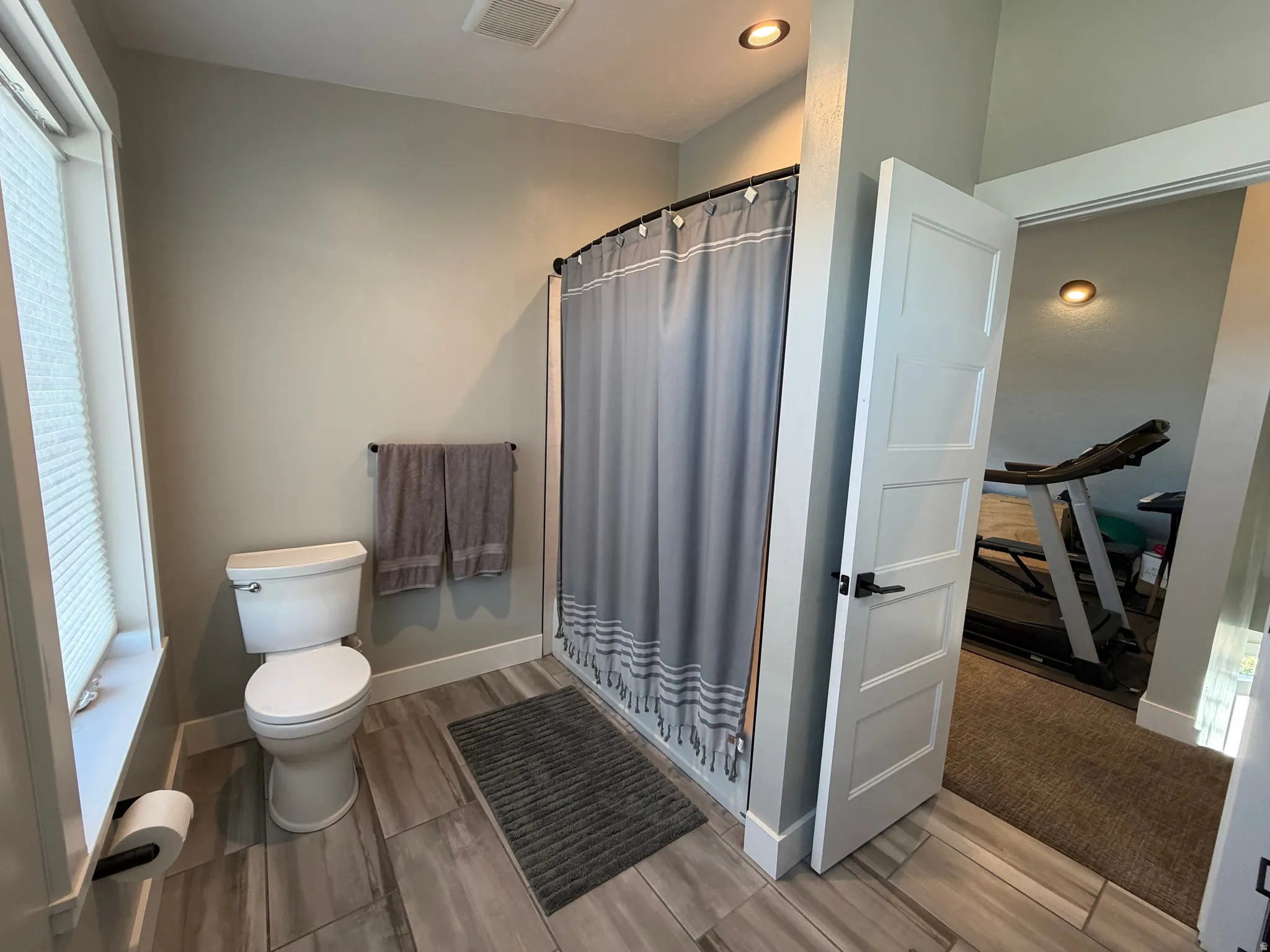 White toilet with a built-in toilet paper holder, recessed ceiling lighting, and a towel bar