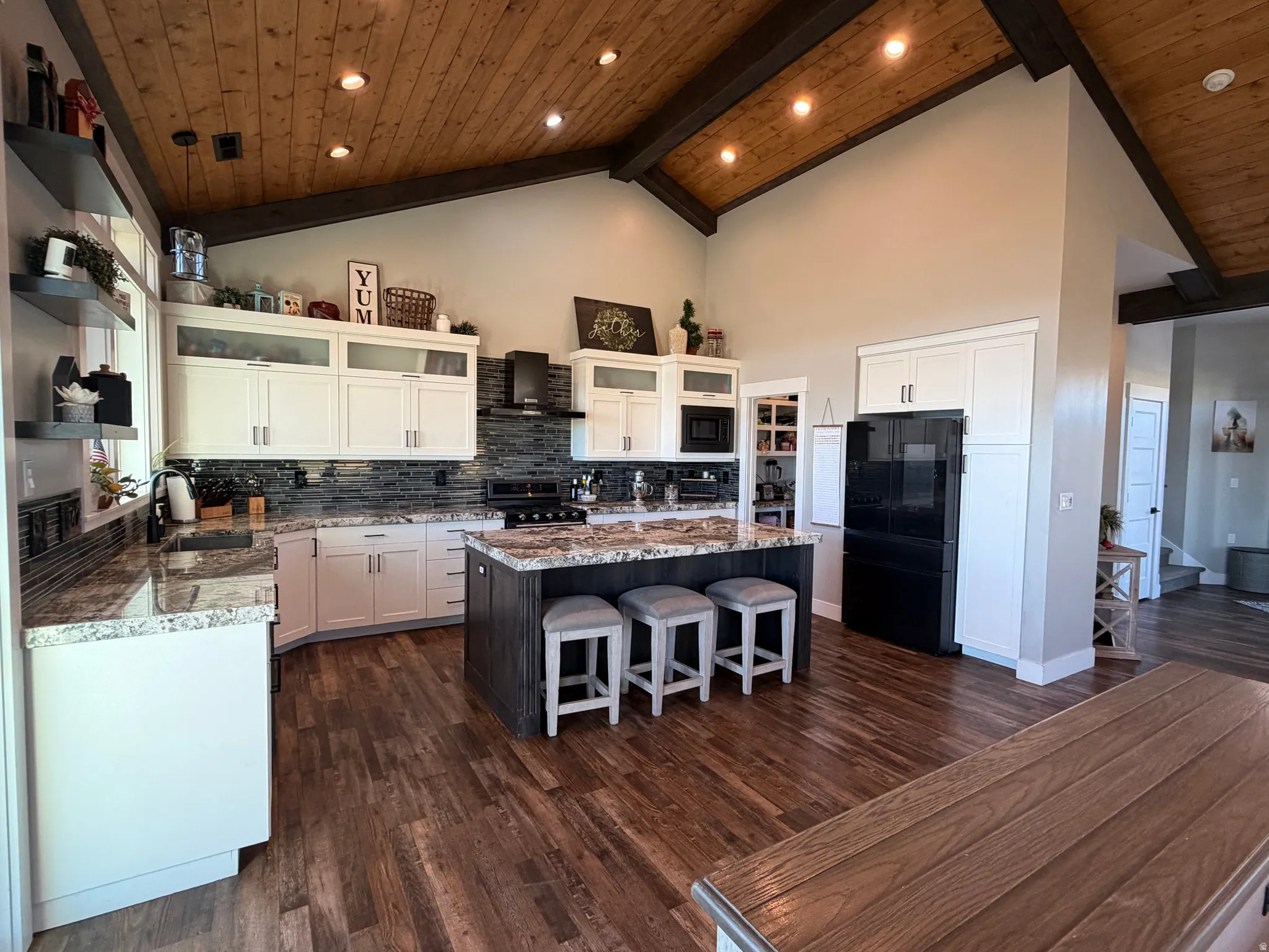Vaulted wood-finish ceiling with exposed beams, wood-finish flooring, white cabinetry with integrated appliances, stone countertops, and a central island with bar seating