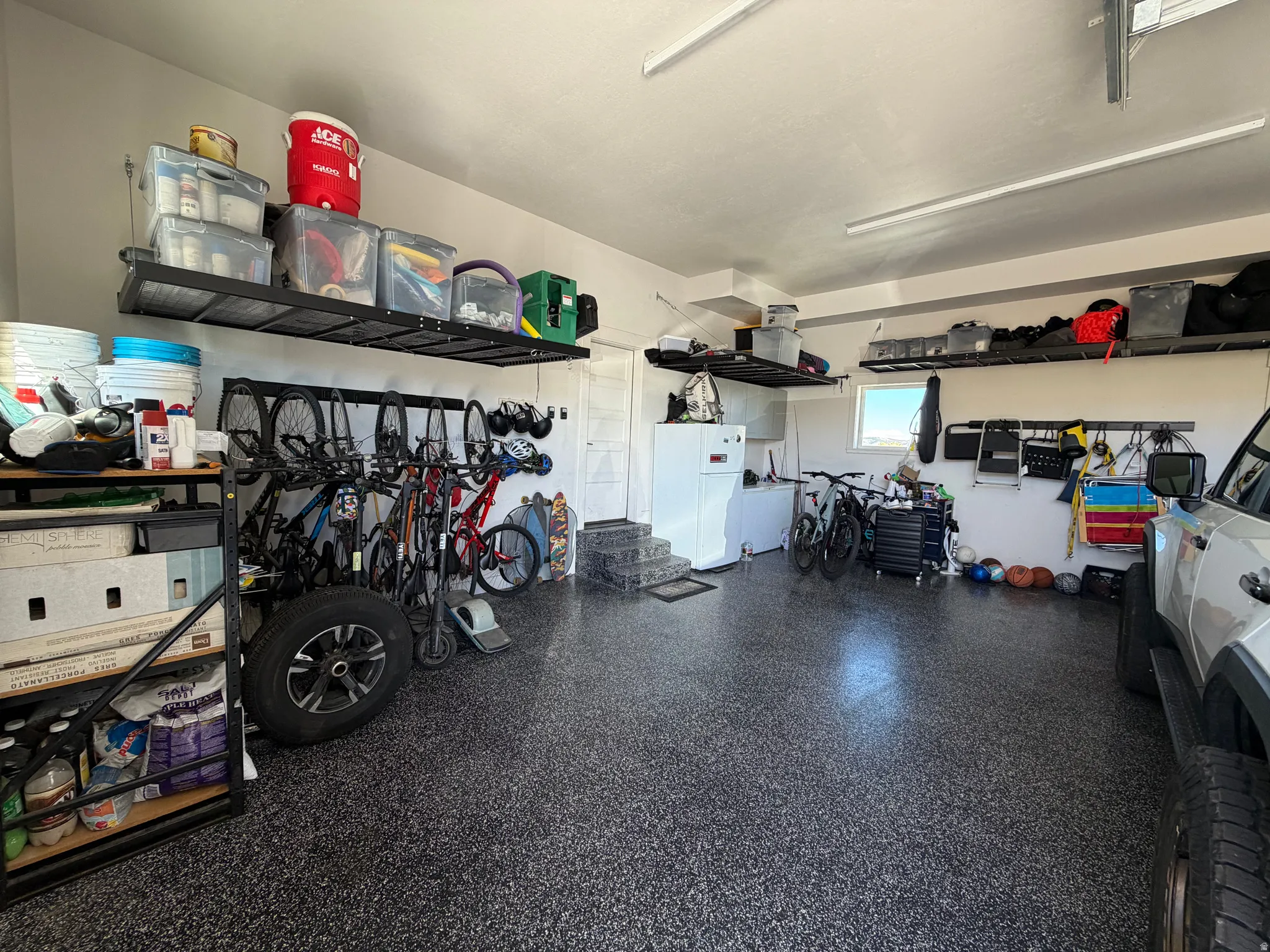 Garage featuring an epoxy coated floor, overhead metal shelving, and wall-mounted storage racks