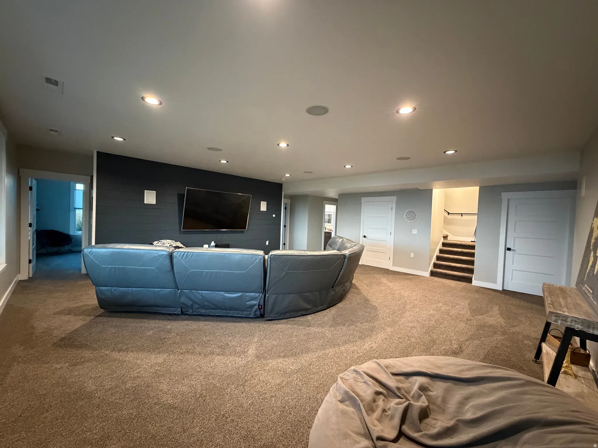 Carpeted flooring throughout, recessed ceiling lighting, a dark accent wall, white paneled doors with black hardware, and a staircase with a dark wood-finish handrail