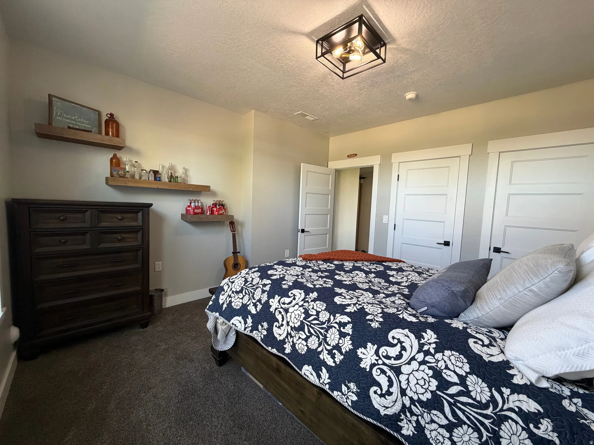Recessed square ceiling light fixture, wall-mounted floating shelves, white paneled doors with black hardware, and gray carpeting