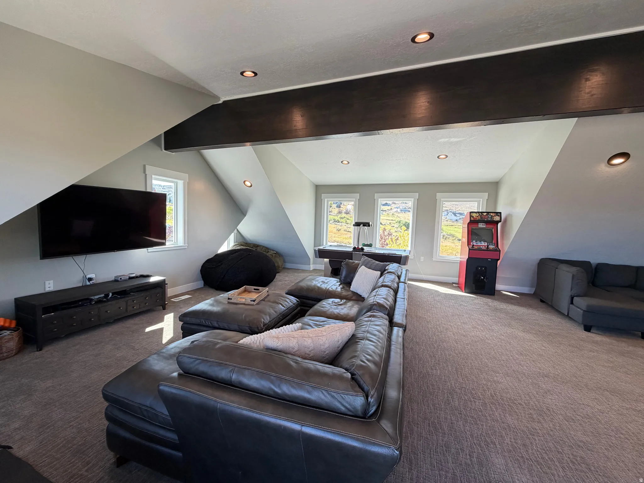 Expansive carpeted room featuring multiple windows, recessed lighting, and a prominent ceiling beam