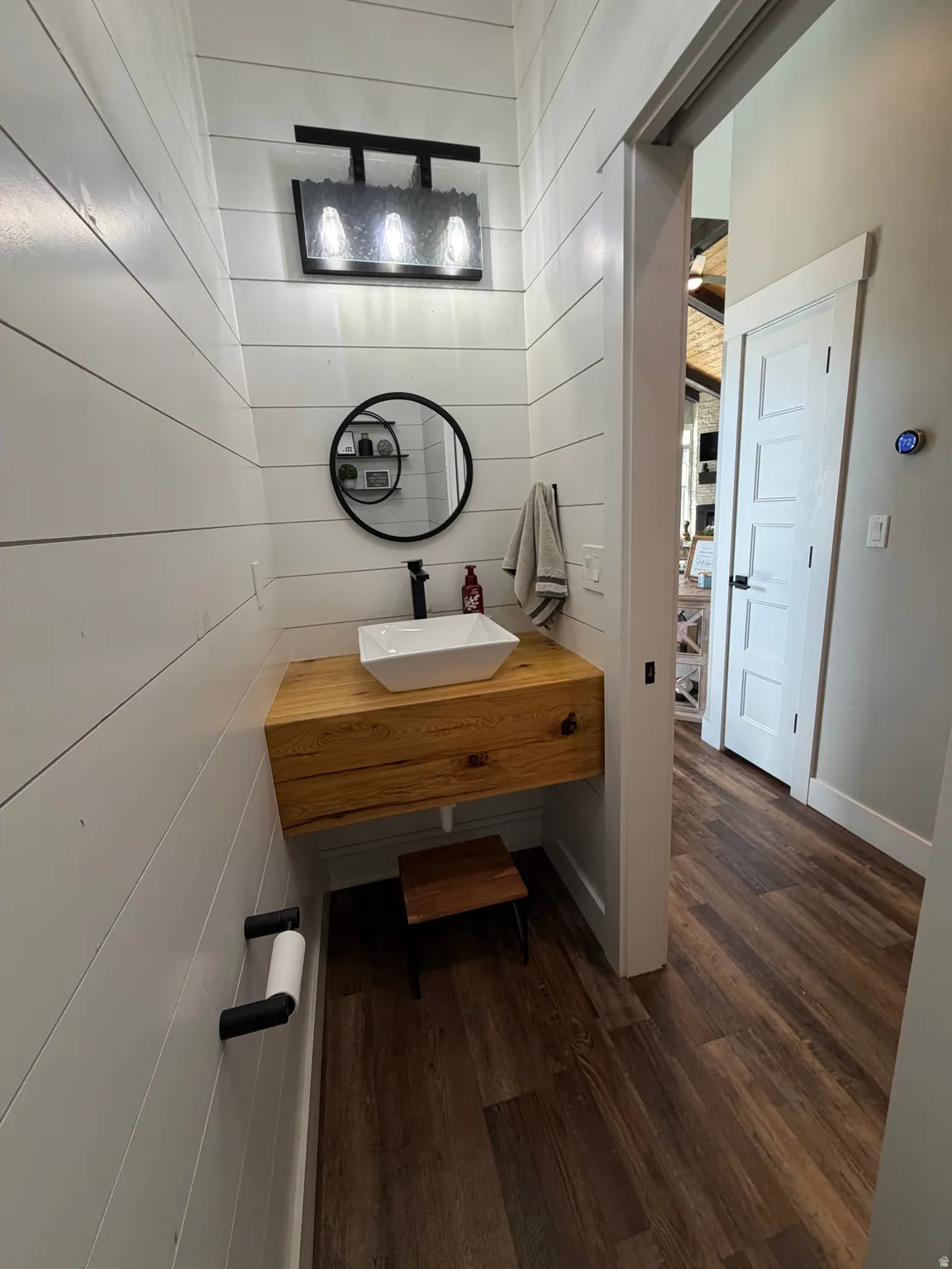 Shiplap wall paneling, wood-finish flooring, floating wood-finish vanity, rectangular vessel sink, and a modern black wall-mounted faucet