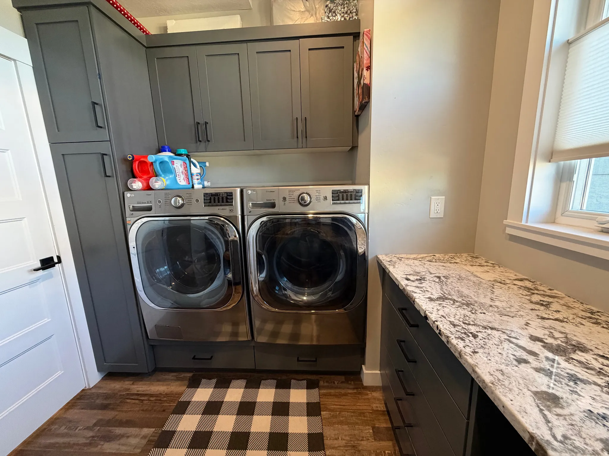 Laundry area featuring wood-finish flooring, dark cabinetry, and stone countertops