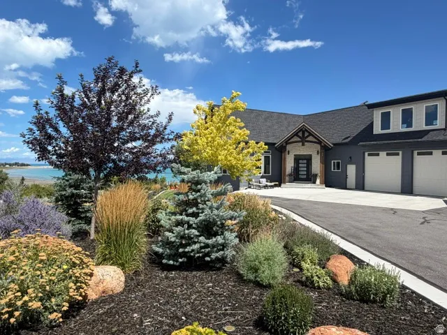 Contemporary exterior with a covered entry, stone accents, a three-car garage, and mature landscaping