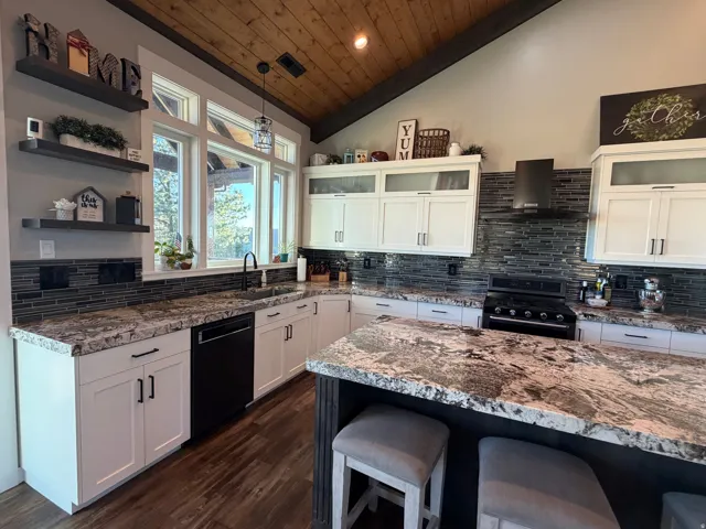 Vaulted wood-finish ceiling, white cabinetry with dark hardware, stone countertops, dark tile backsplash, and wood-finish flooring