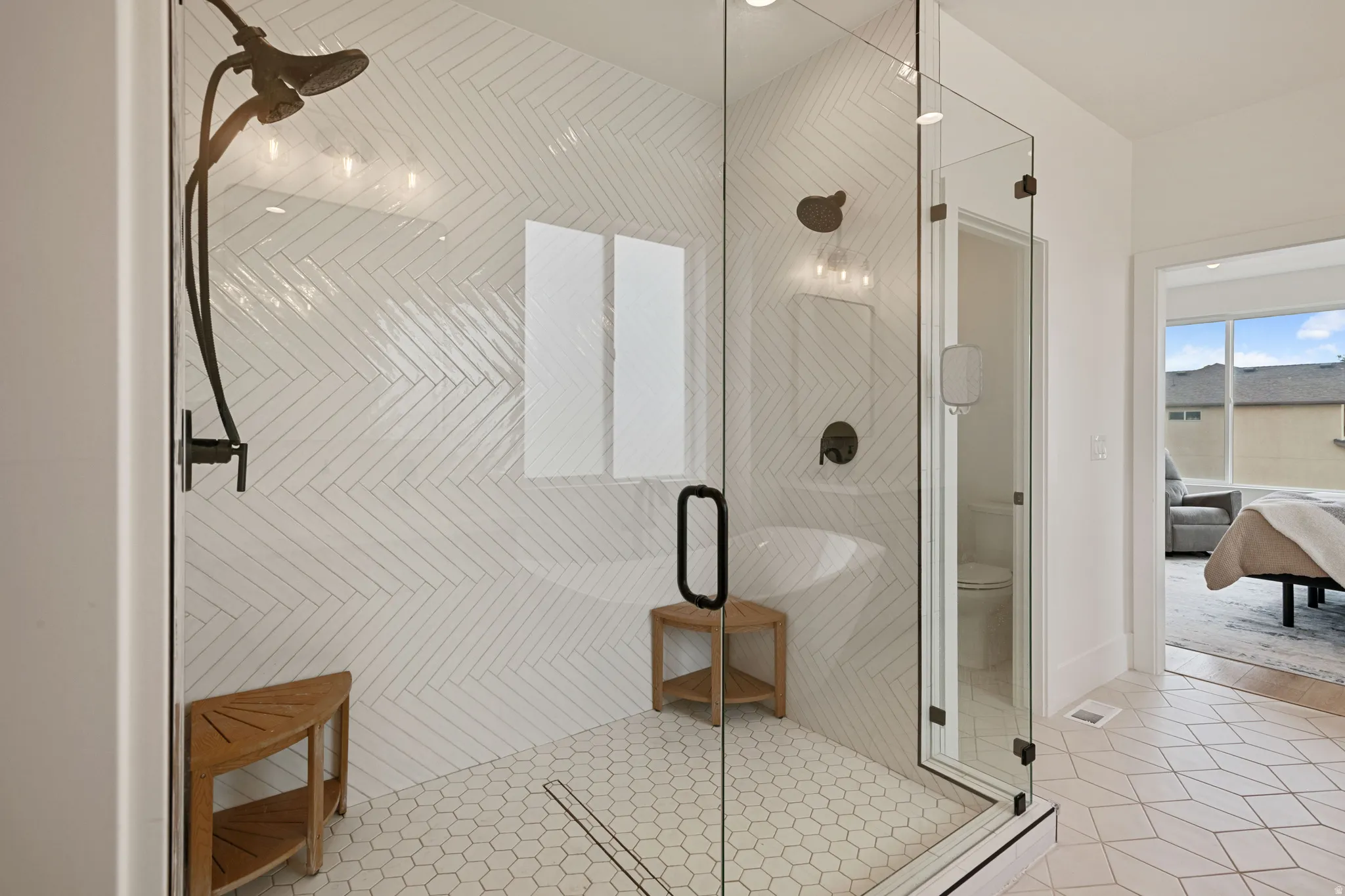 Glass-enclosed shower with a dark bronze rainfall shower head, herringbone tile shower surround, hexagon tile flooring, and a linear drain