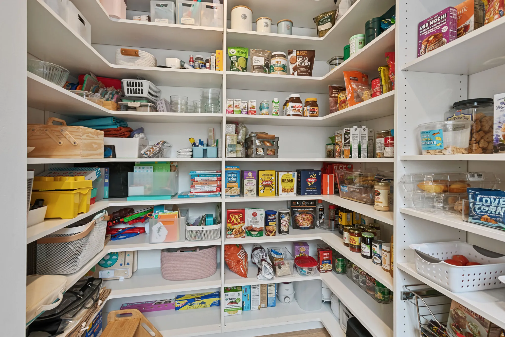 Expansive walk-in pantry featuring white shelving, adjustable shelving, and corner storage solutions
