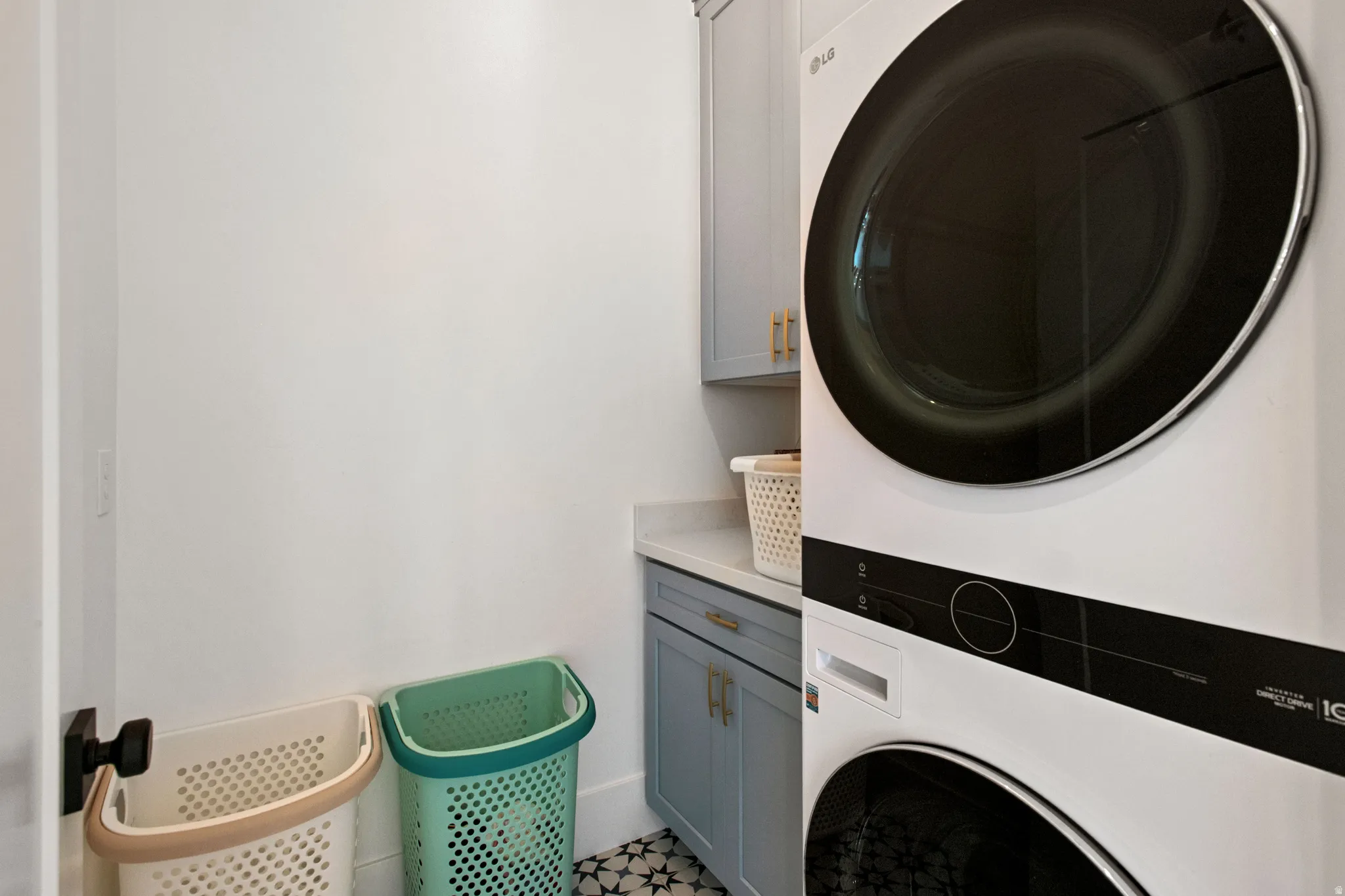 Stackable washer and dryer, light gray cabinetry, light countertop, and patterned floor tile